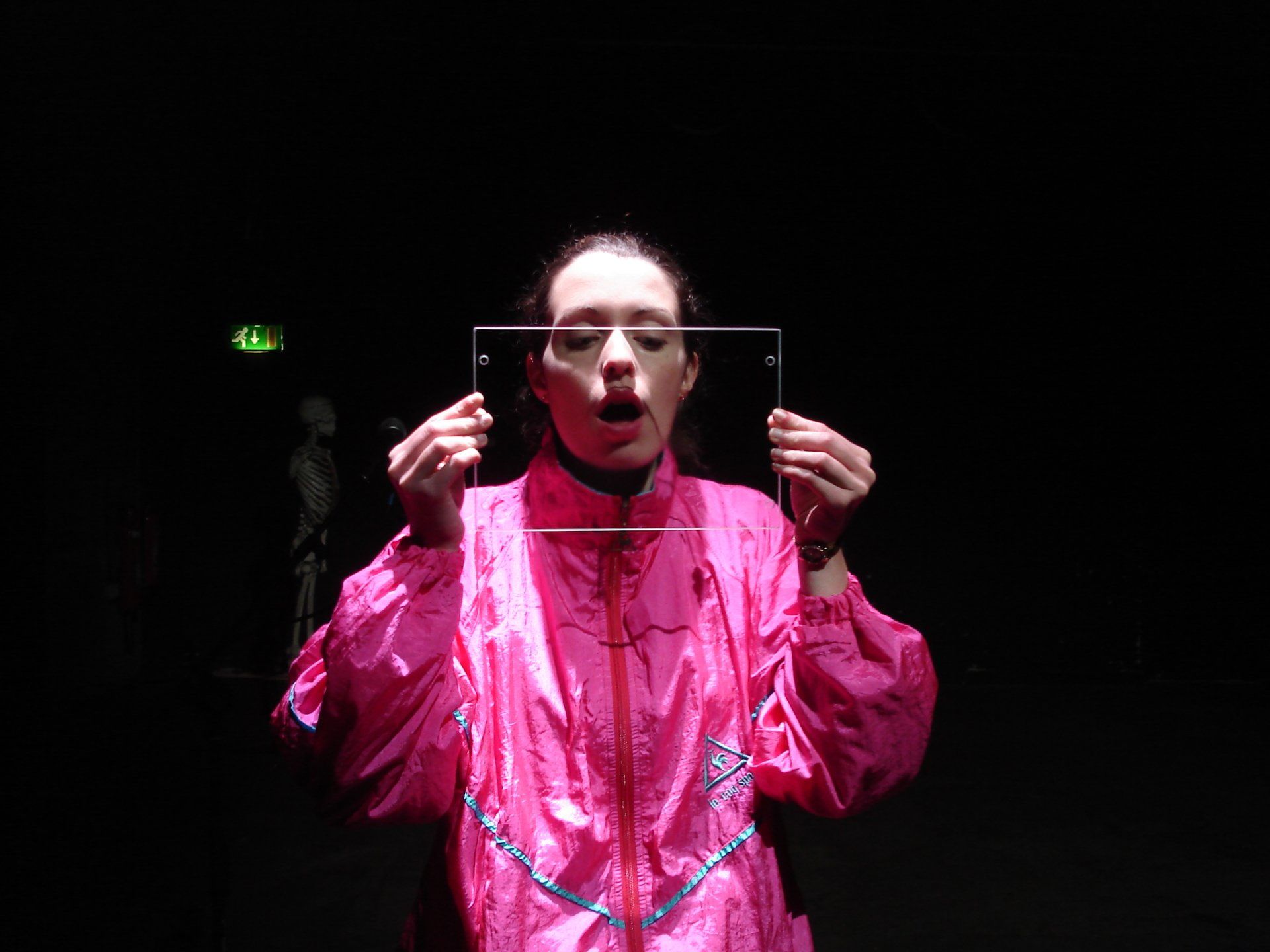 A woman in a pink jacket is holding a piece of glass in front of her face.