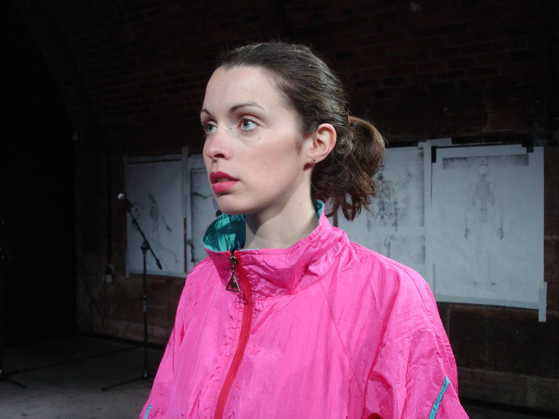 A woman in a pink jacket is standing in front of a microphone.