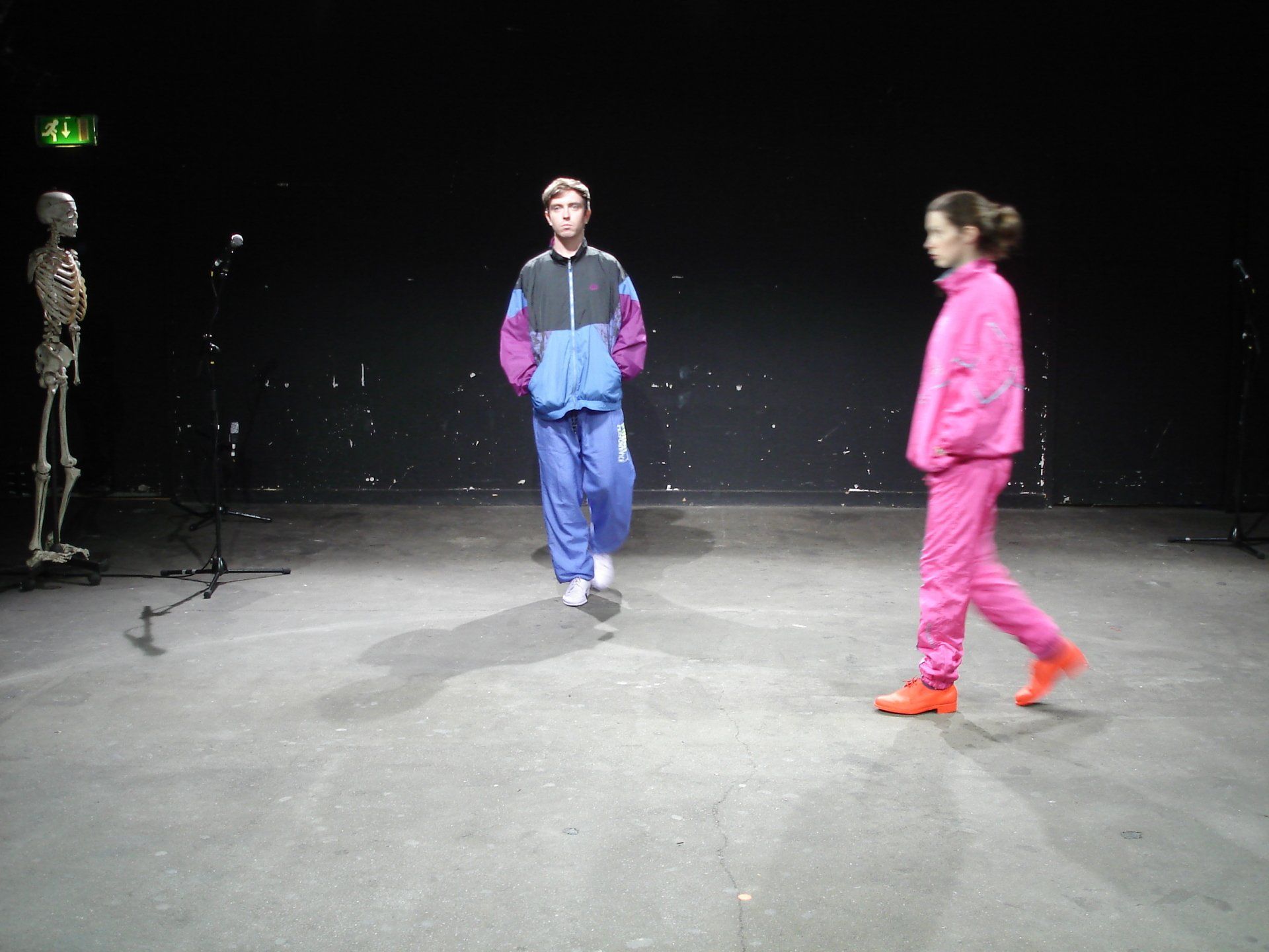 A man and a woman are walking on a stage with a skeleton in the background
