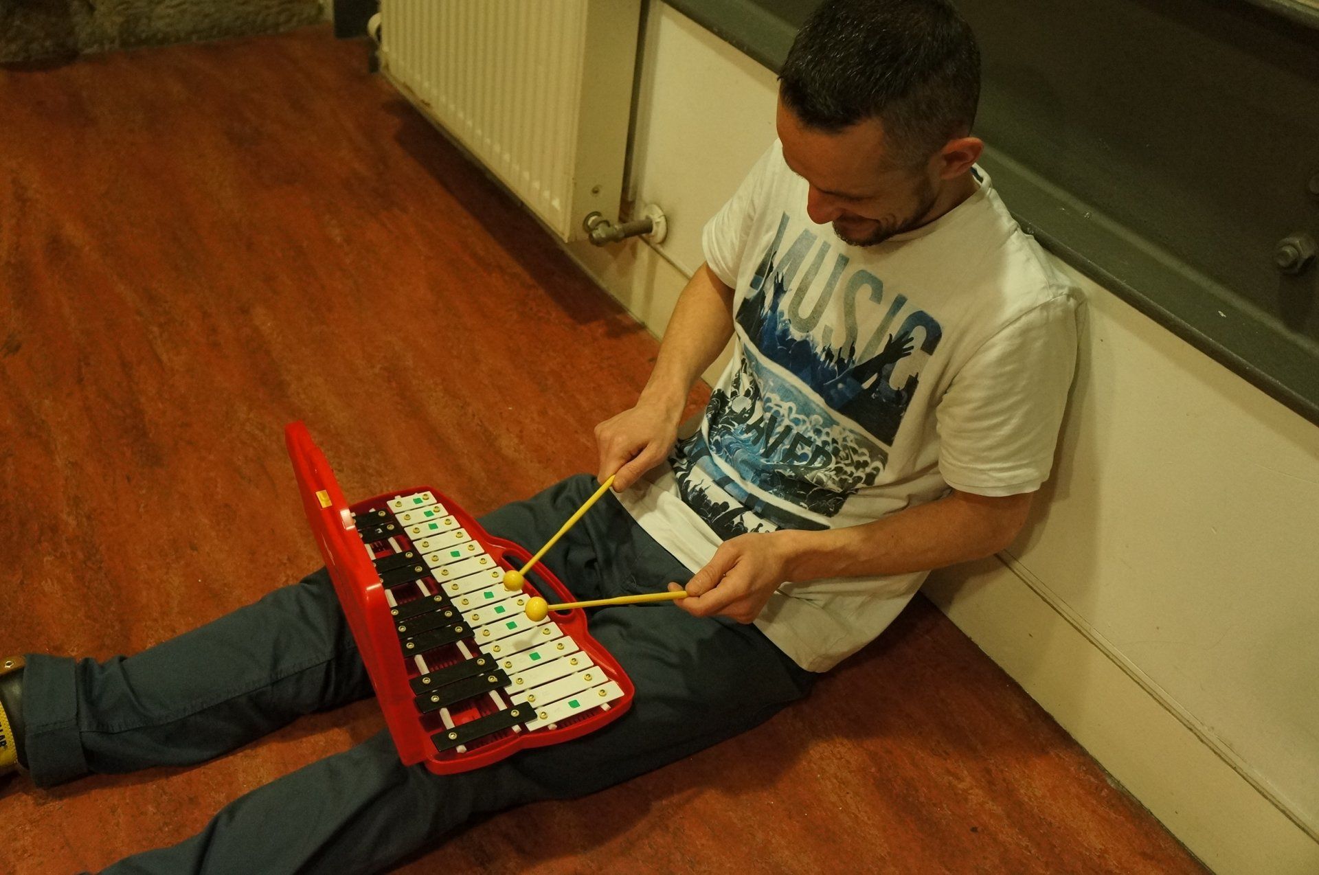 A man is sitting on the floor playing a toy glockenspiel.