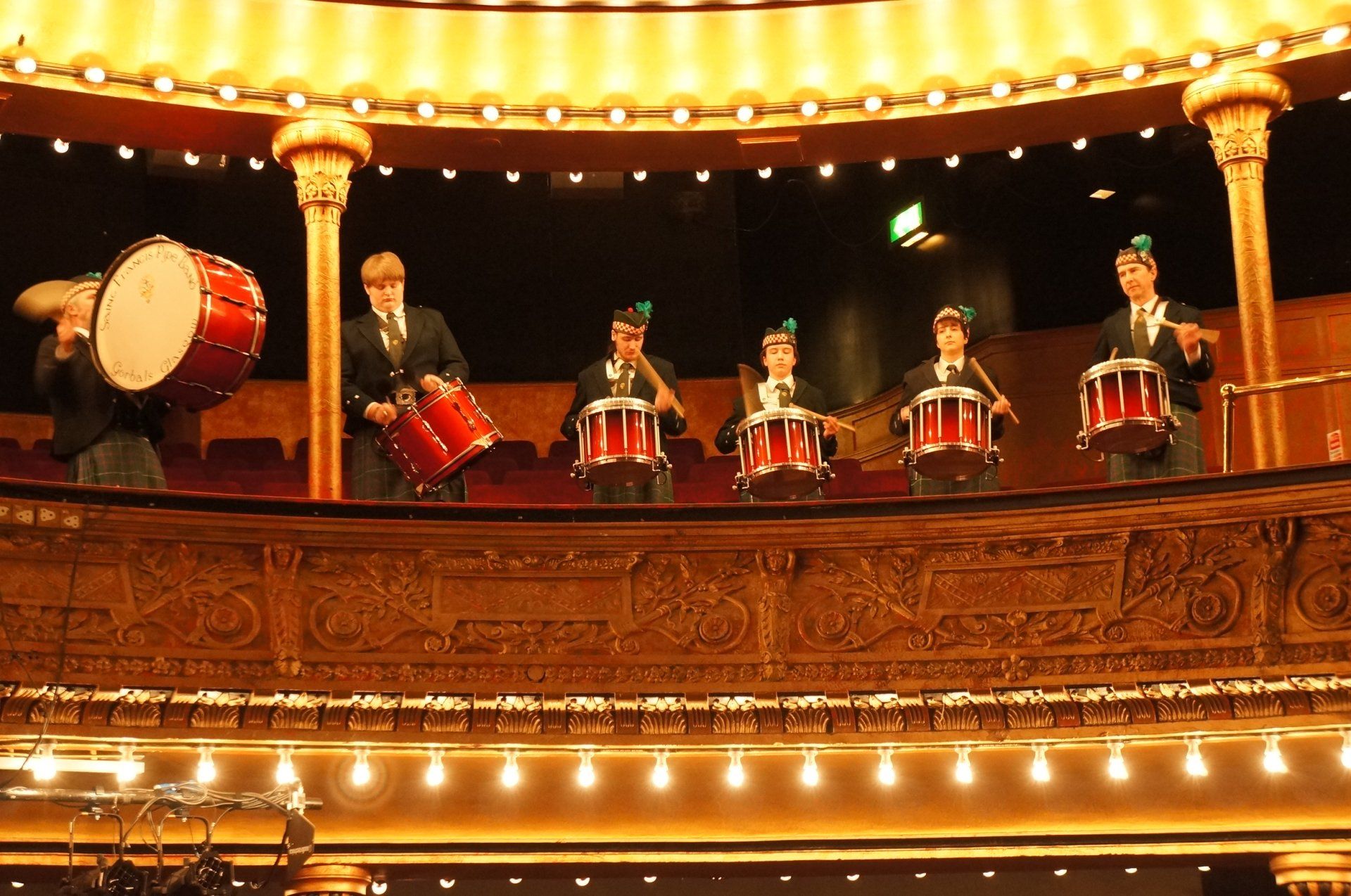 A group of people are playing drums and bagpipes in an auditorium