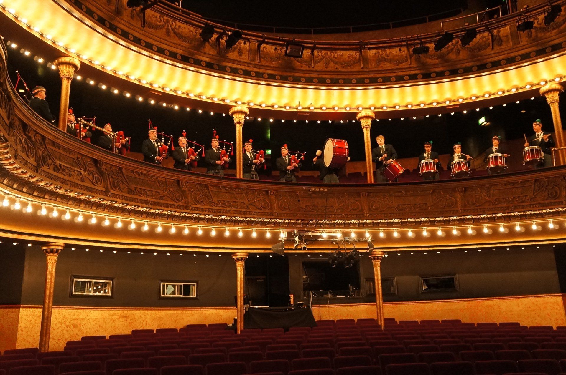 A group of people are playing drums and bagpipes in an auditorium