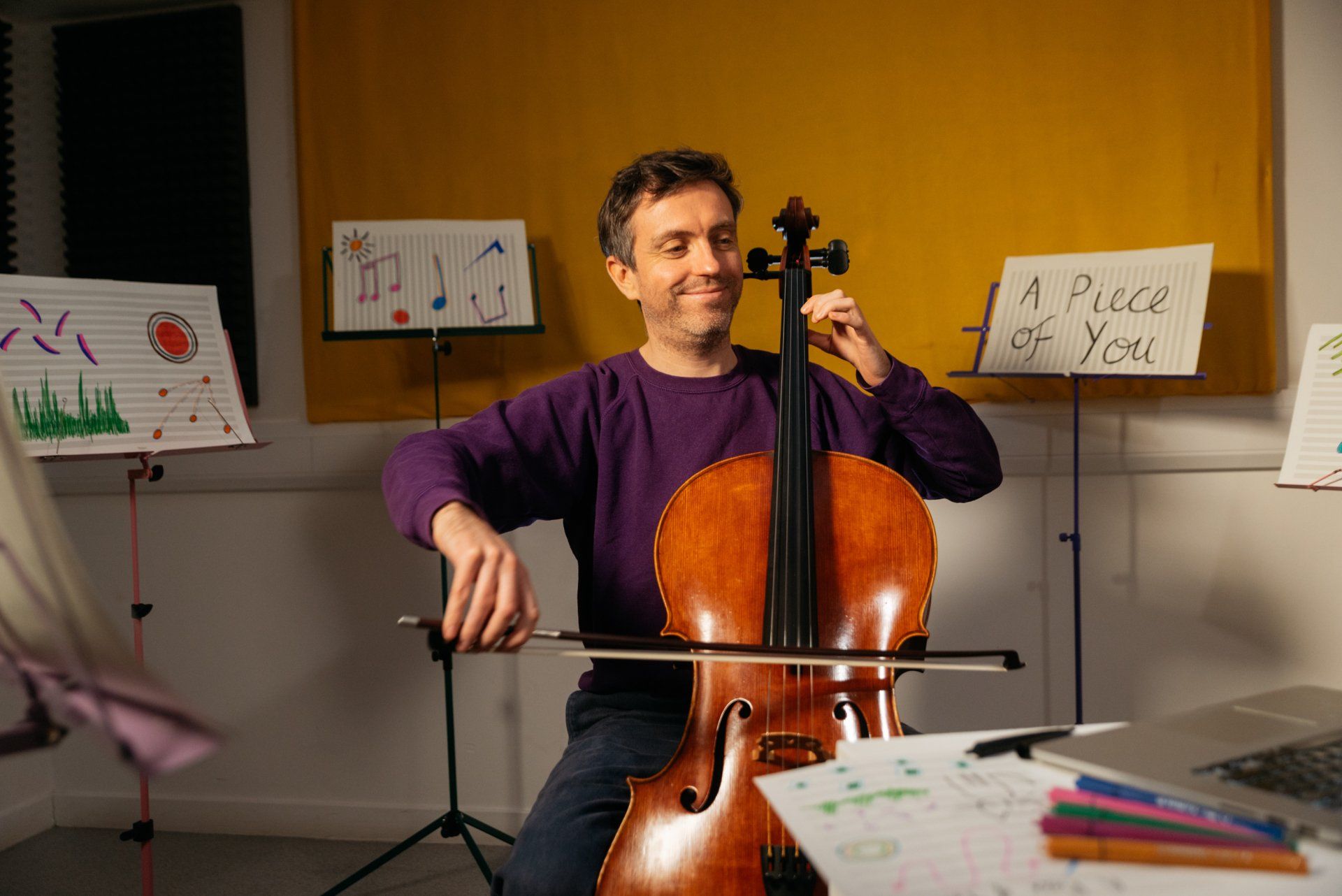 A man in a purple sweater is playing a cello.