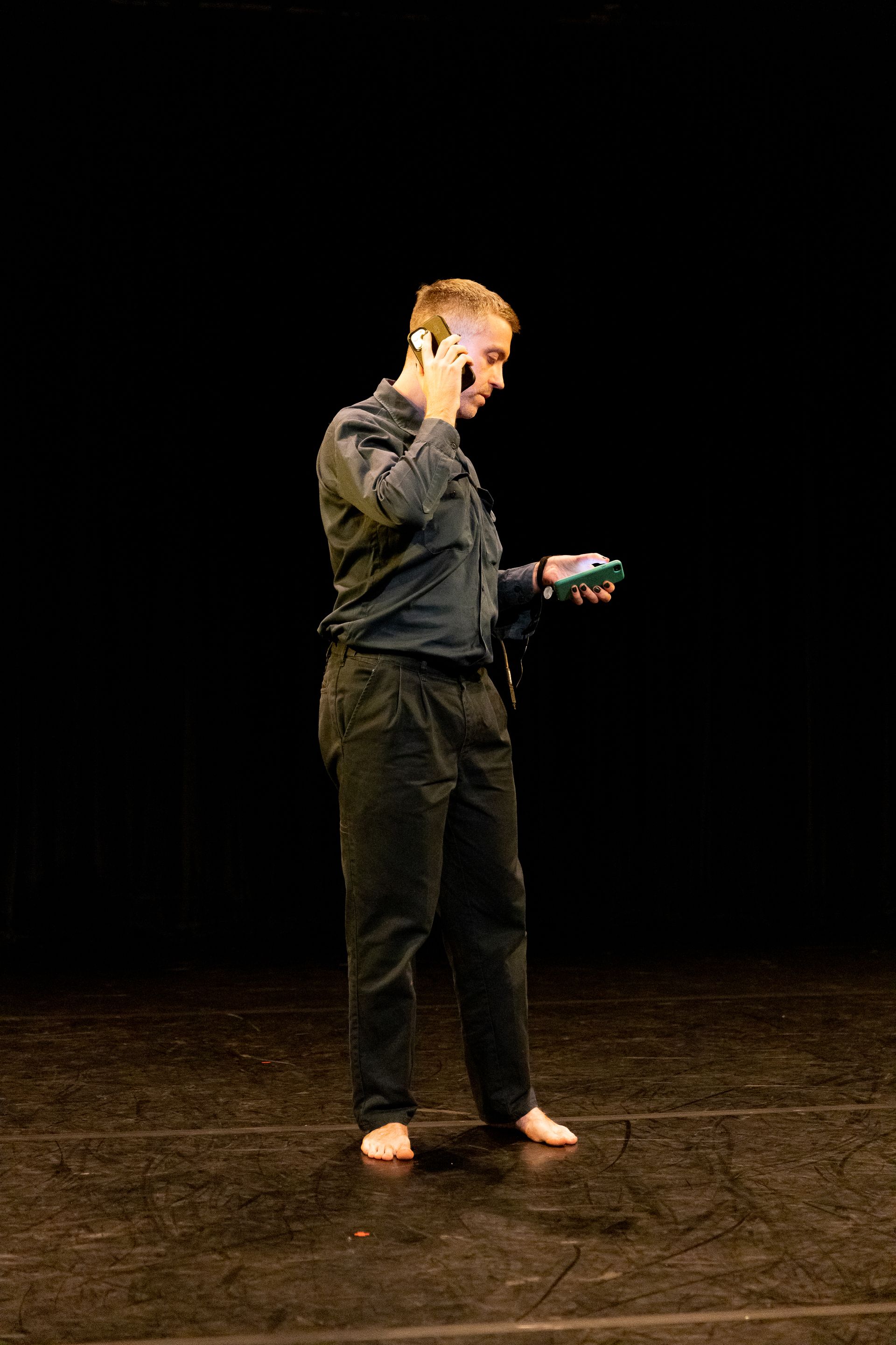 A man is standing on a stage holding two mobile phones.