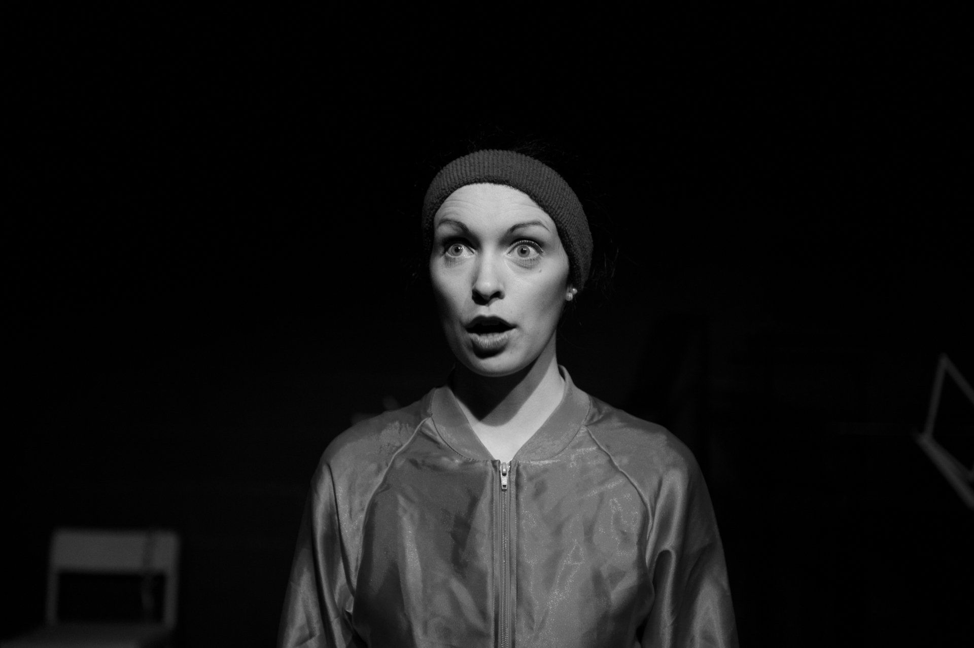 A black and white photo of a woman wearing a beanie and a satin jacket.