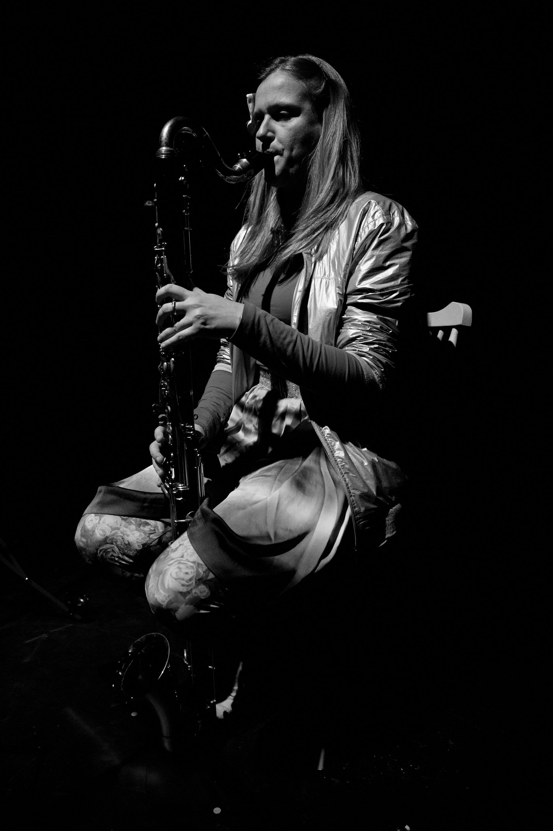 A woman is playing a bass clarinet in a black and white photo.