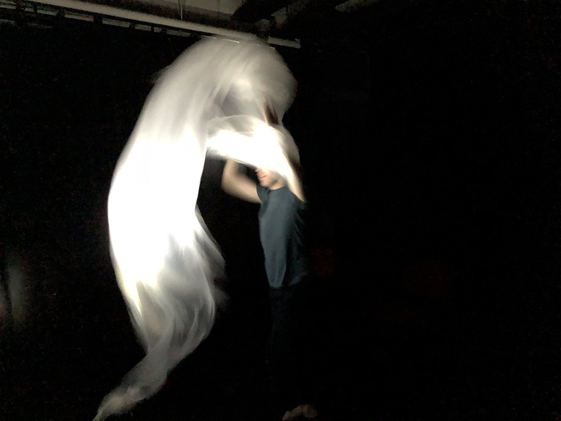 A person is standing in the dark with a white cloth flying in the air