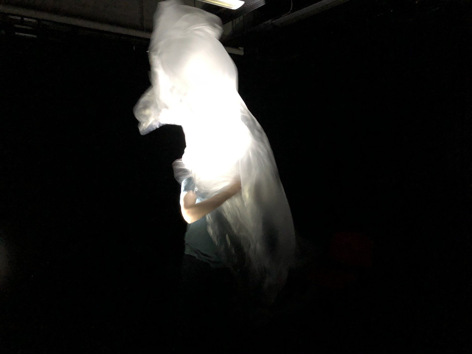 A person is standing in the dark with a white cloth hanging from the ceiling.