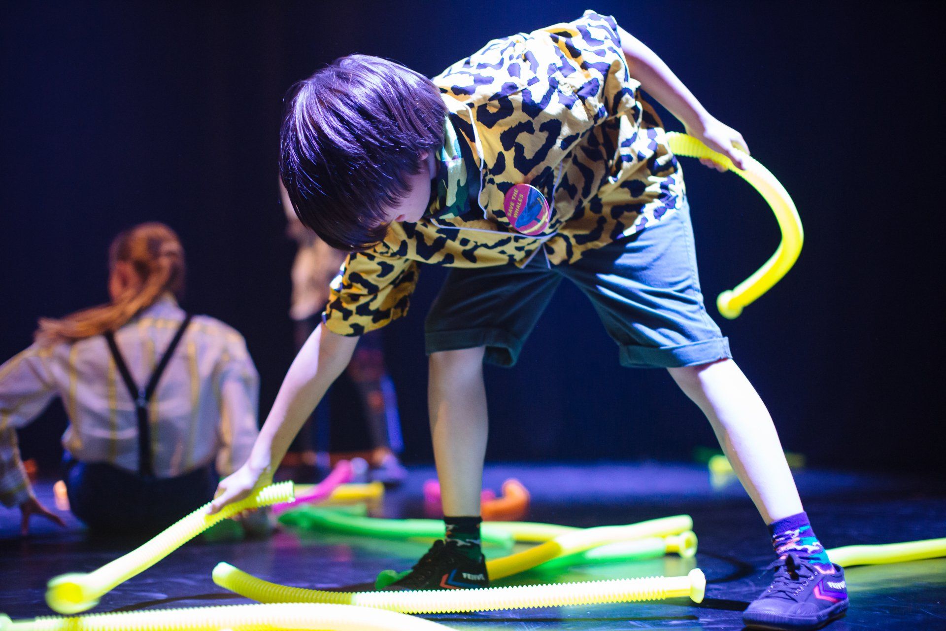A young boy is playing with a bunch of yellow sticks on a stage