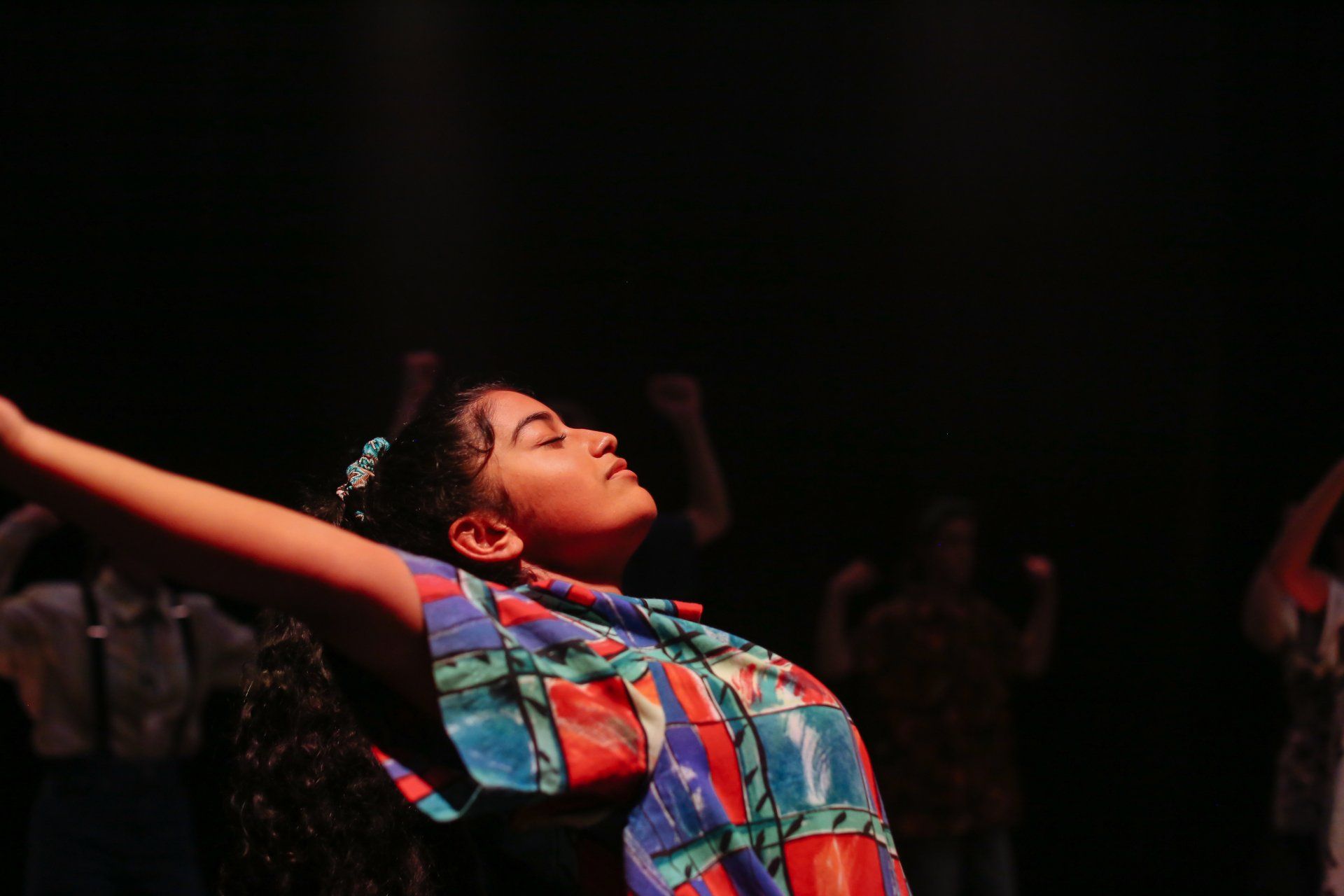 A girl is dancing in a dark room with her arms outstretched.