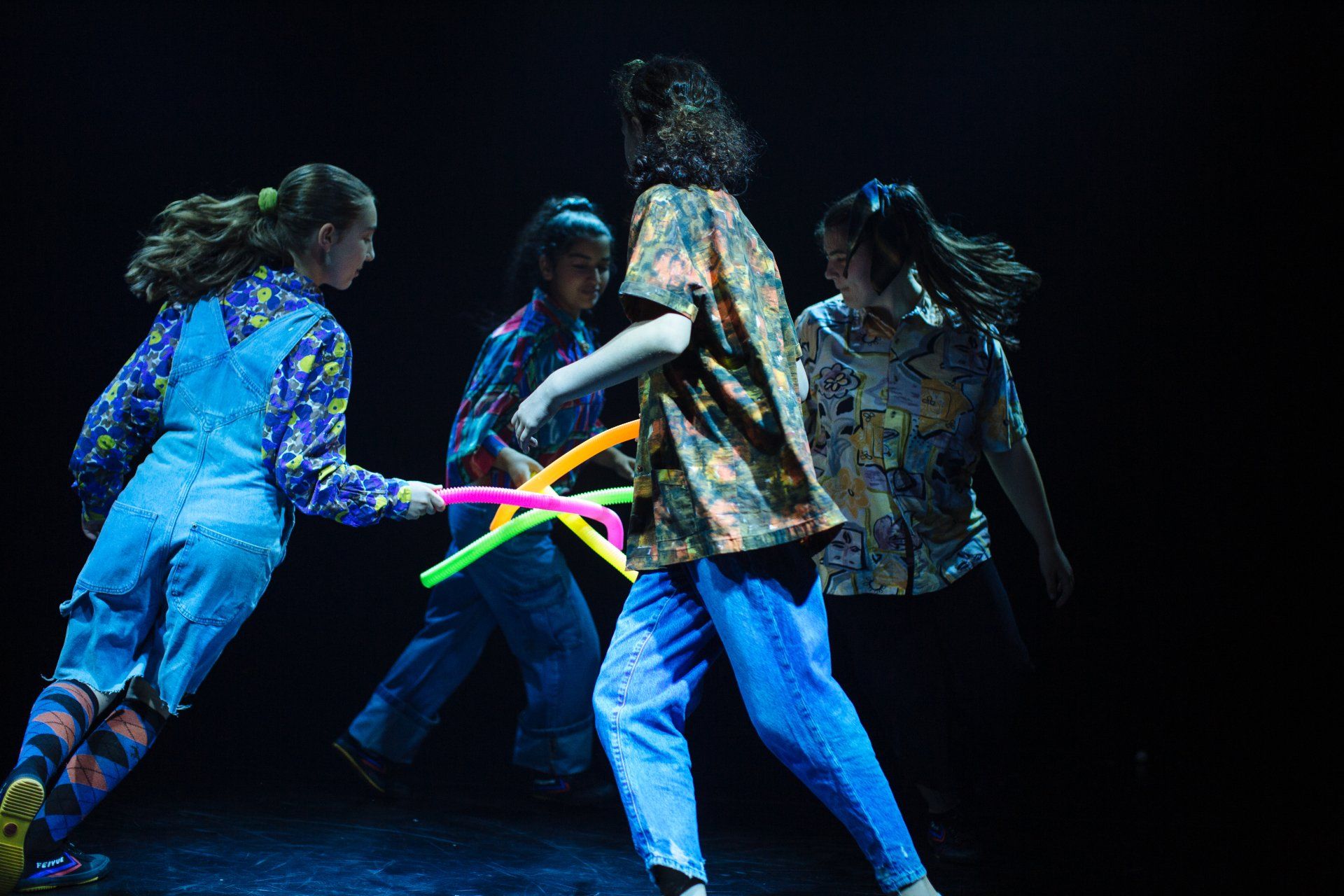 A group of children are playing with colourful tubes on a stage.
