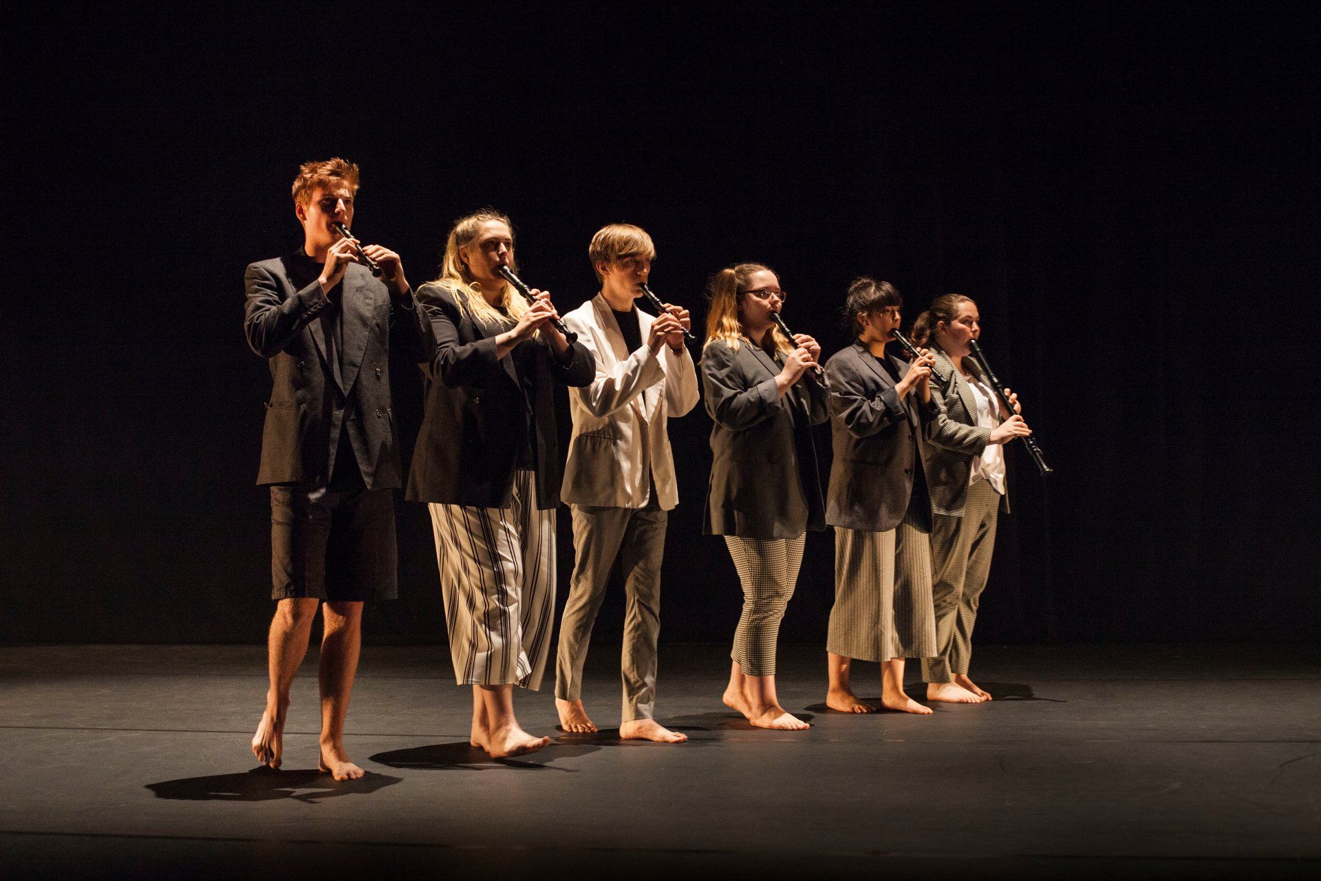 A group of people are standing in a row on a stage playing recorders.