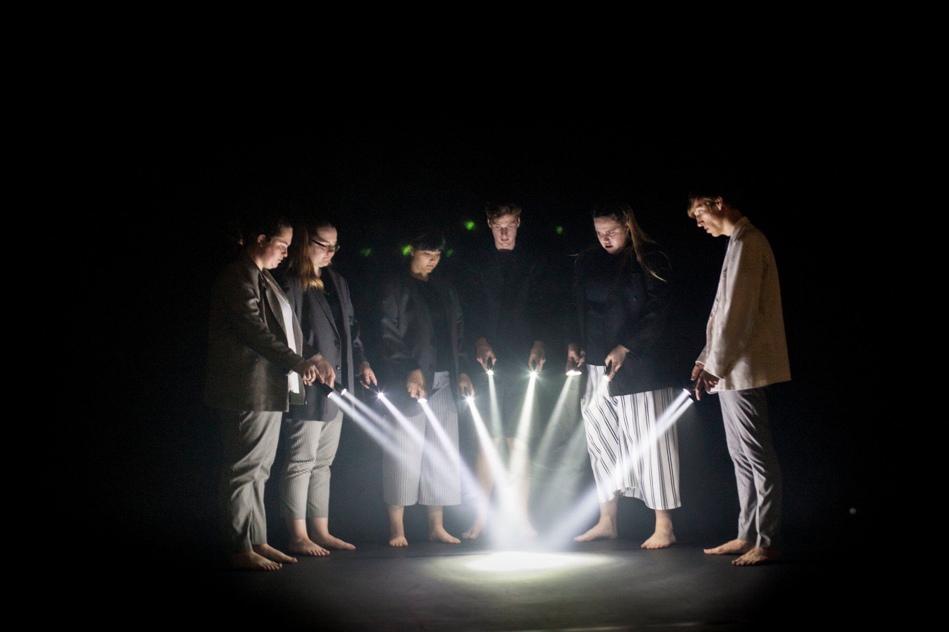 A group of people are standing in a circle pointing torchlights in the dark.