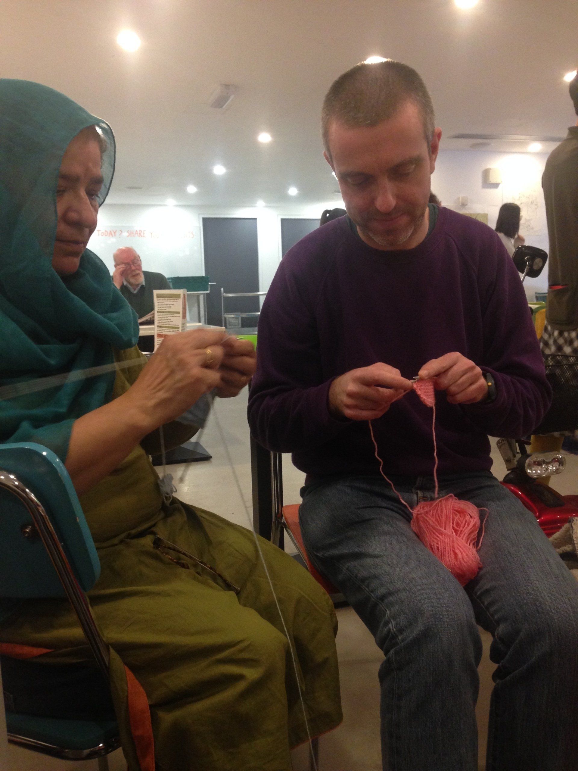 A man and a woman are knitting together in a room