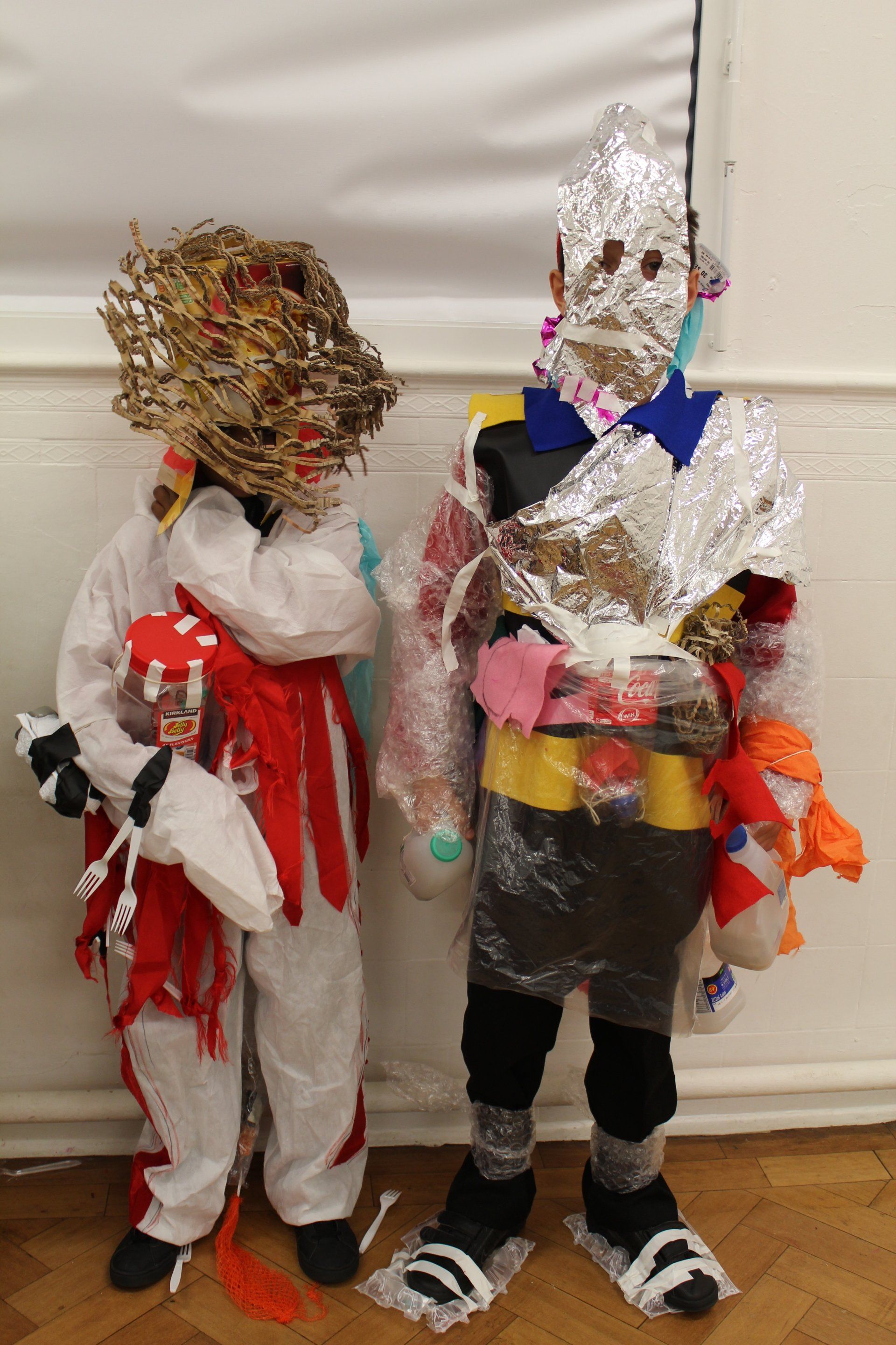 A couple of children standing next to each other wearing costumes made from rubbish.