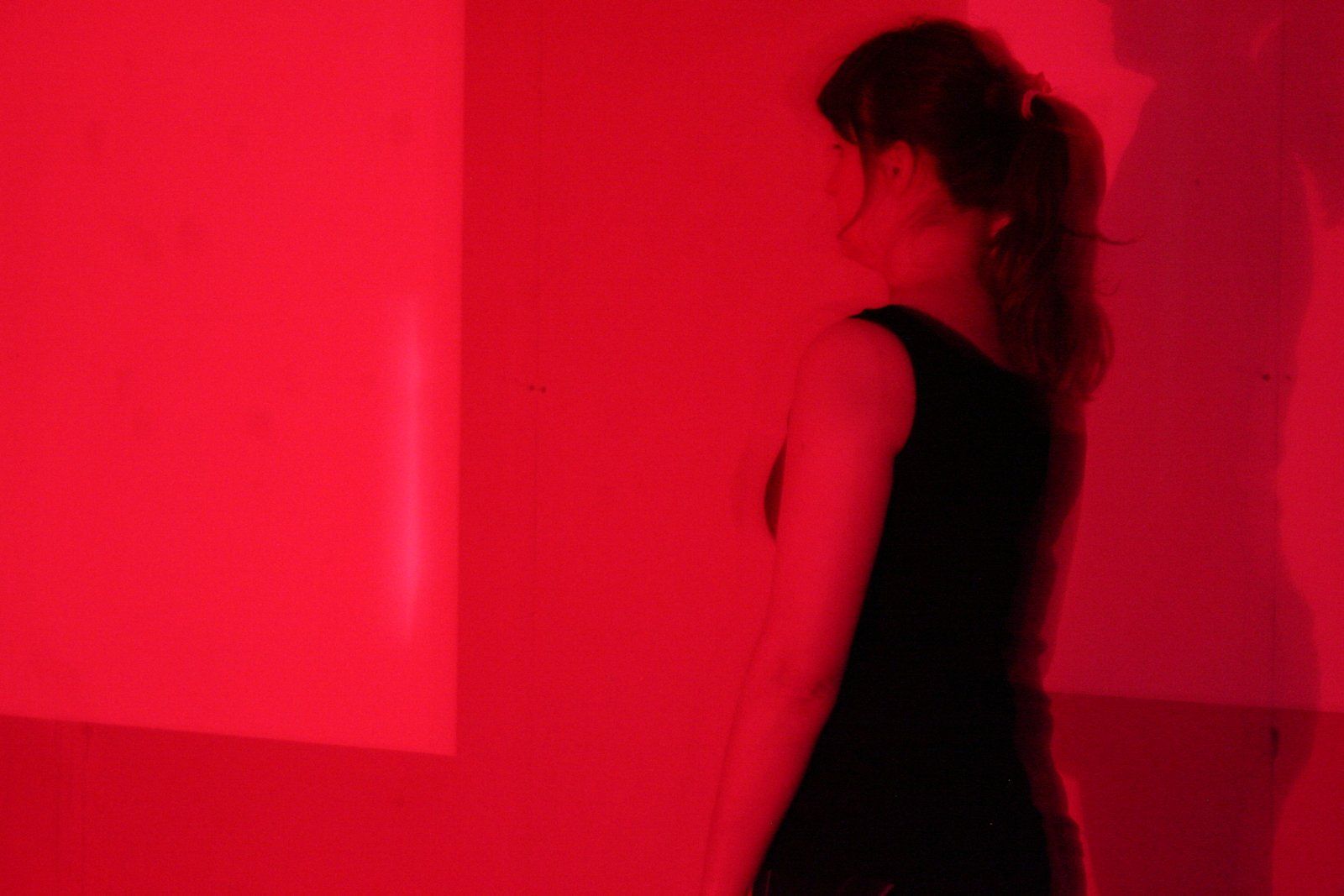 A woman in a black dress is standing in front of a red wall.