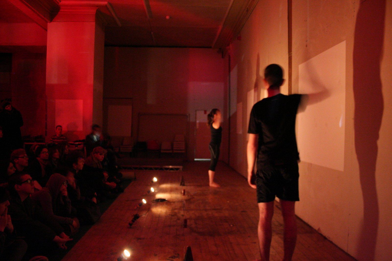 A man and a woman are standing in a dark room with torches and metronomes on the floor..