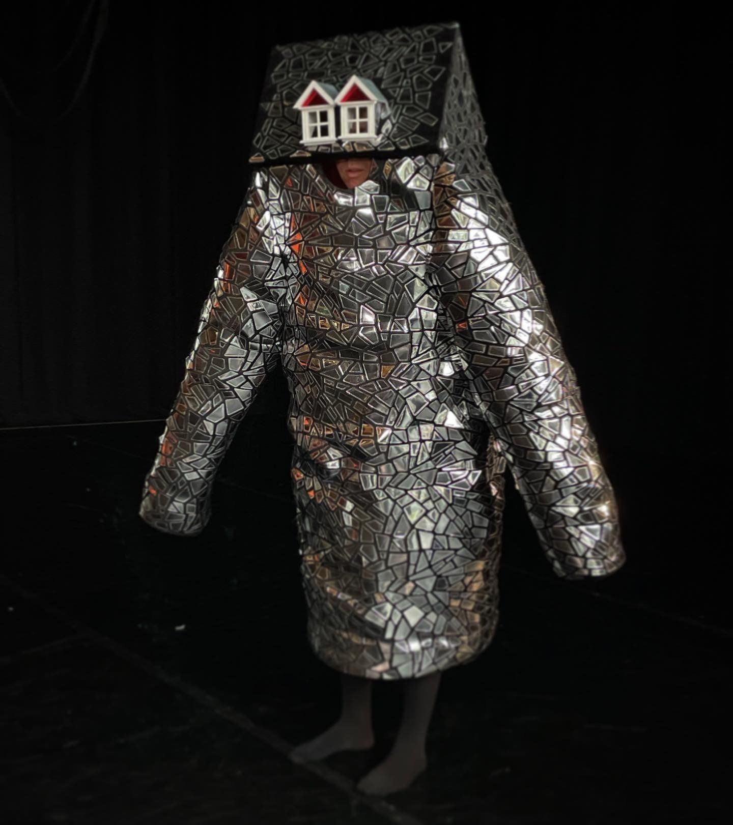 A person in a silver costume with a doll's house on their head
