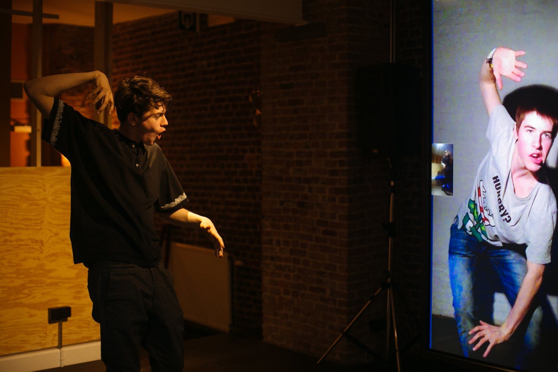 A man is standing in front of a large screen with a picture of a man on it.