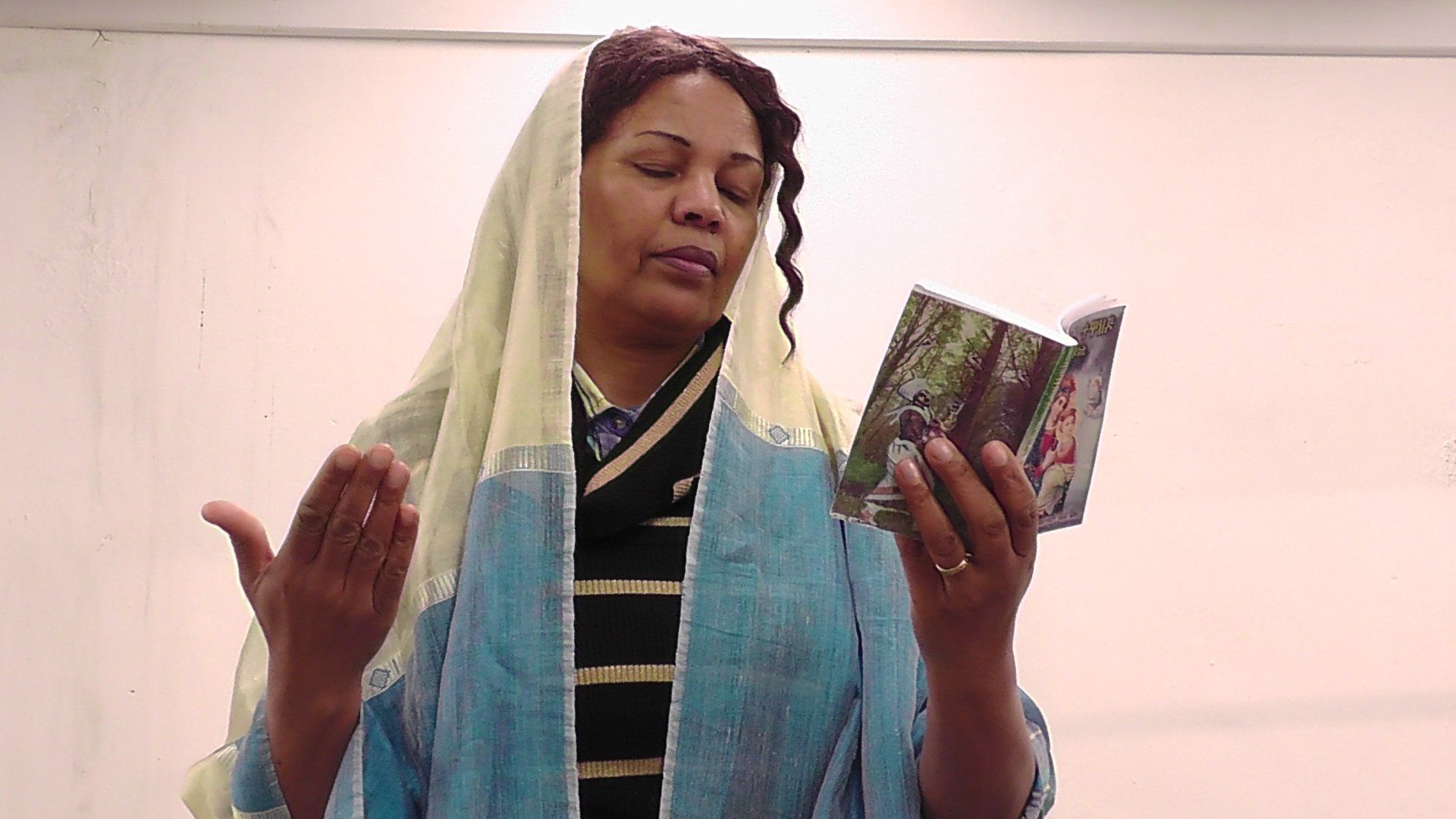 A woman wearing a head scarf is holding a book in her hands.
