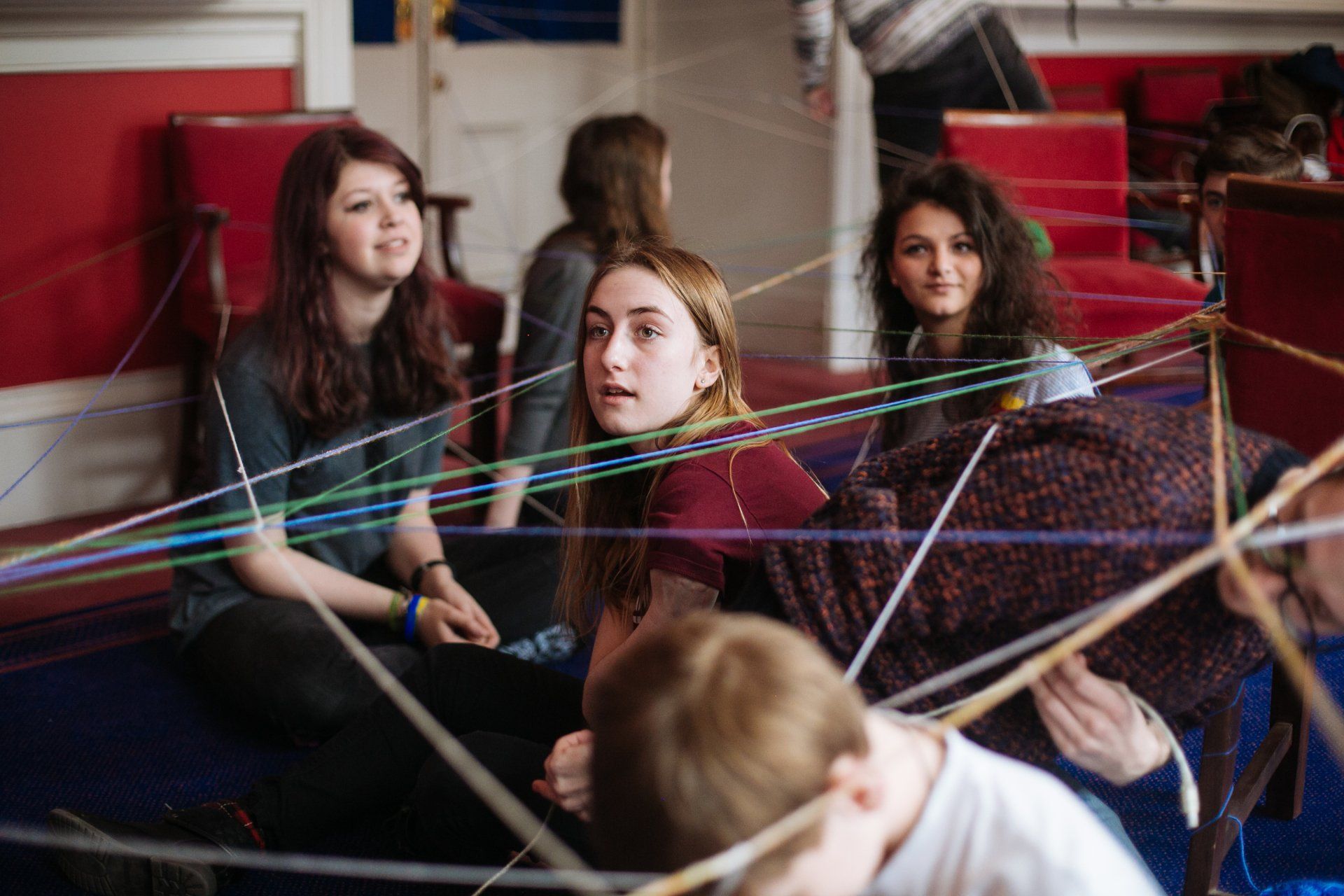 A group of people are sitting on the floor playing with yarn.