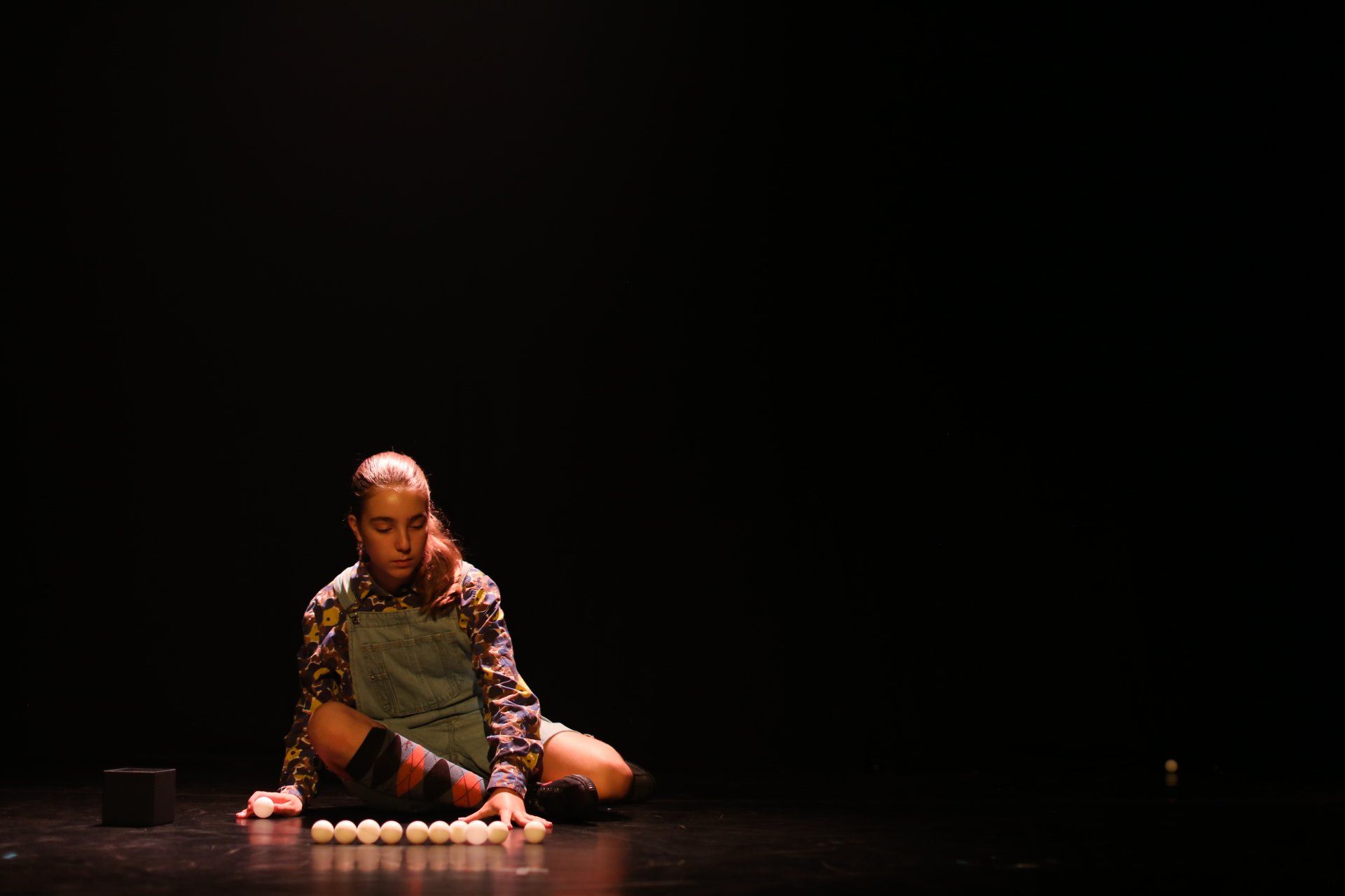 A girl is sitting on the floor on a stage lining up ping pong balls.