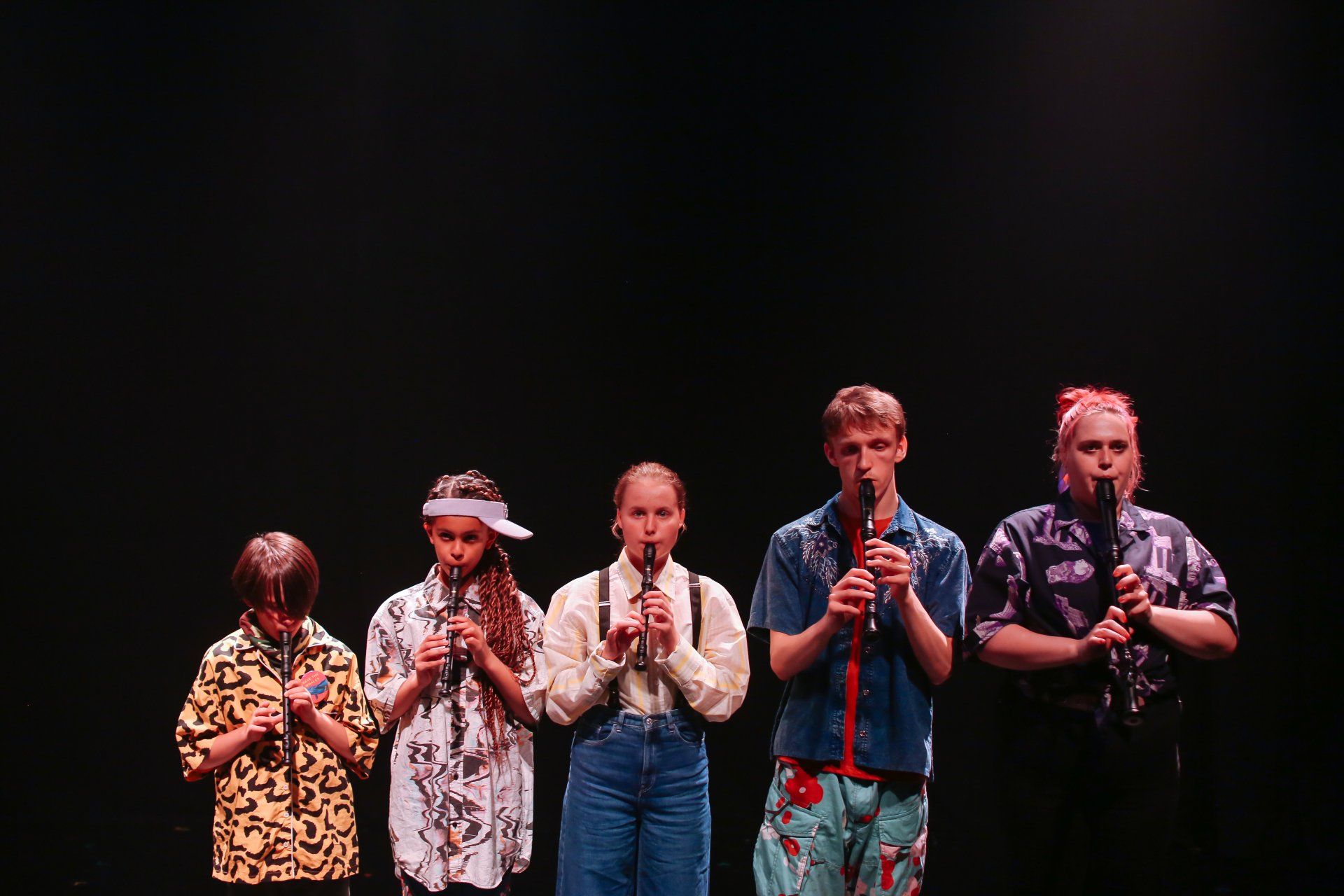 A group of people are standing next to each other on a stage playing recorders.