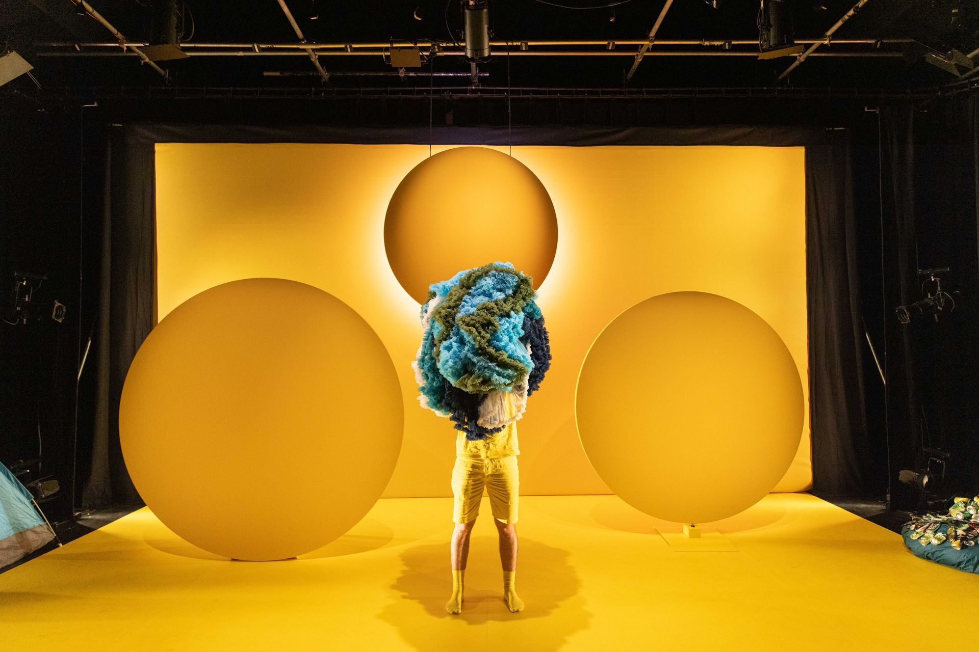 A person is standing on a yellow stage holding a ball of colourful costumes.