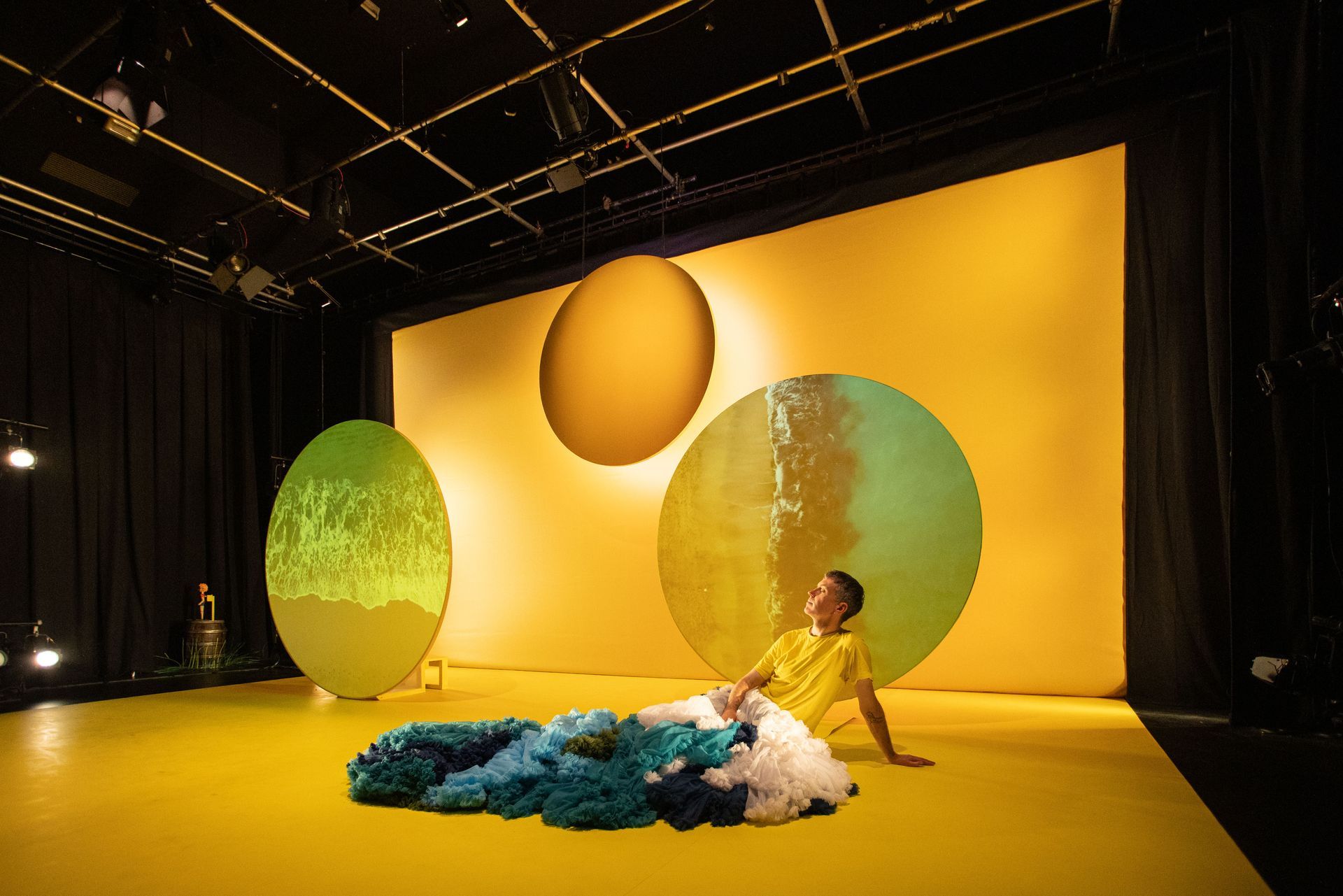 A man in a yellow shirt is sitting on the floor in front of a yellow wall.