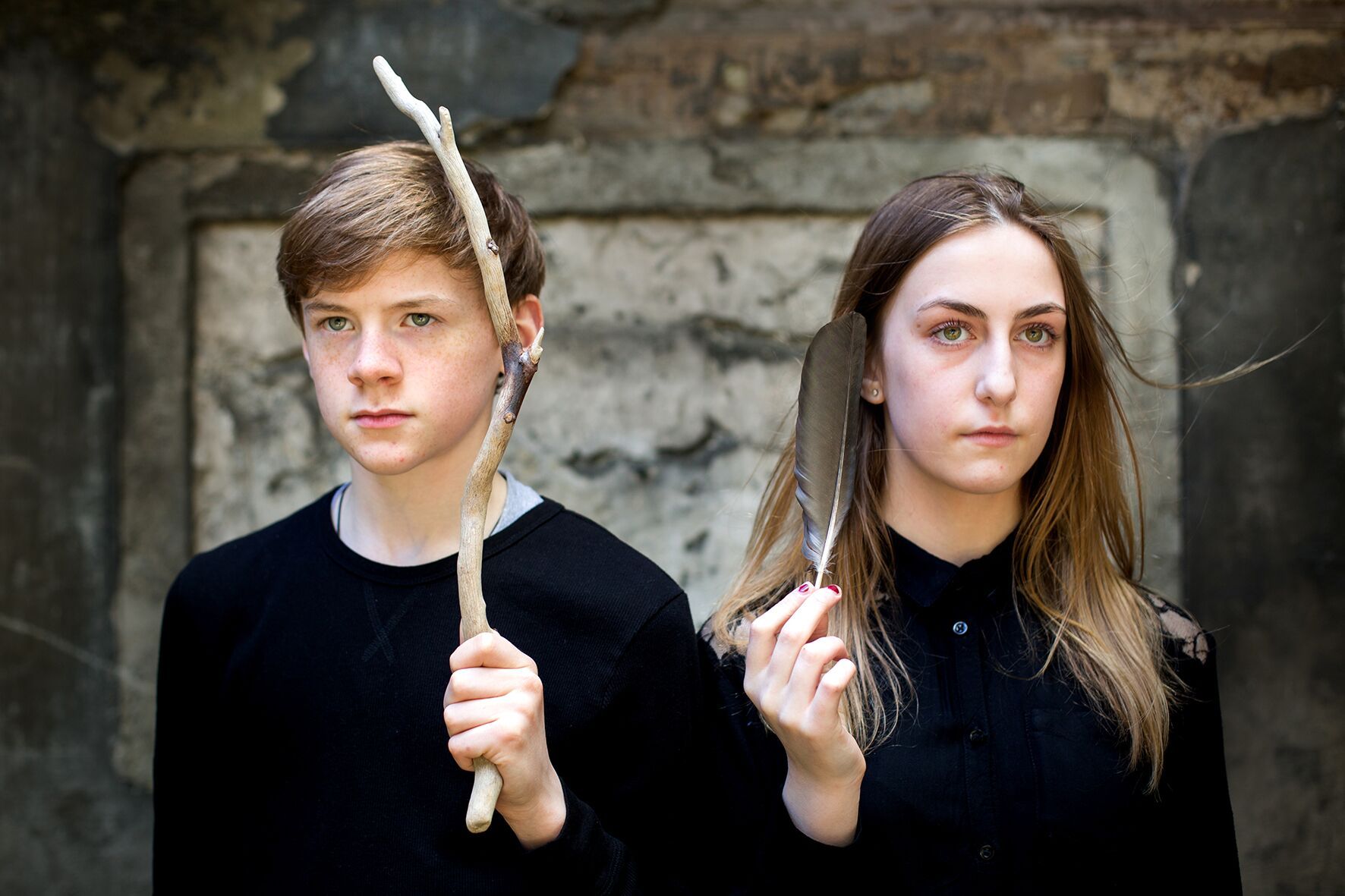 A boy and a girl are standing next to each other holding sticks and feathers.