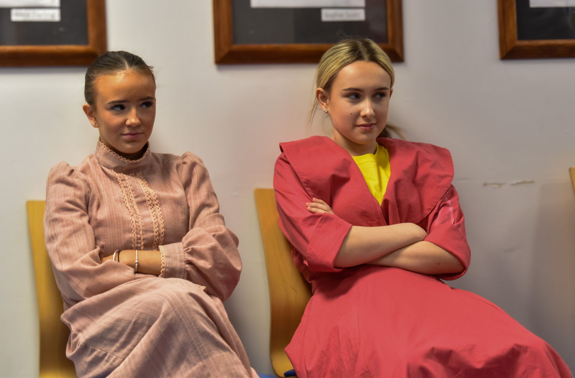 Two girls are sitting in chairs with their arms crossed.