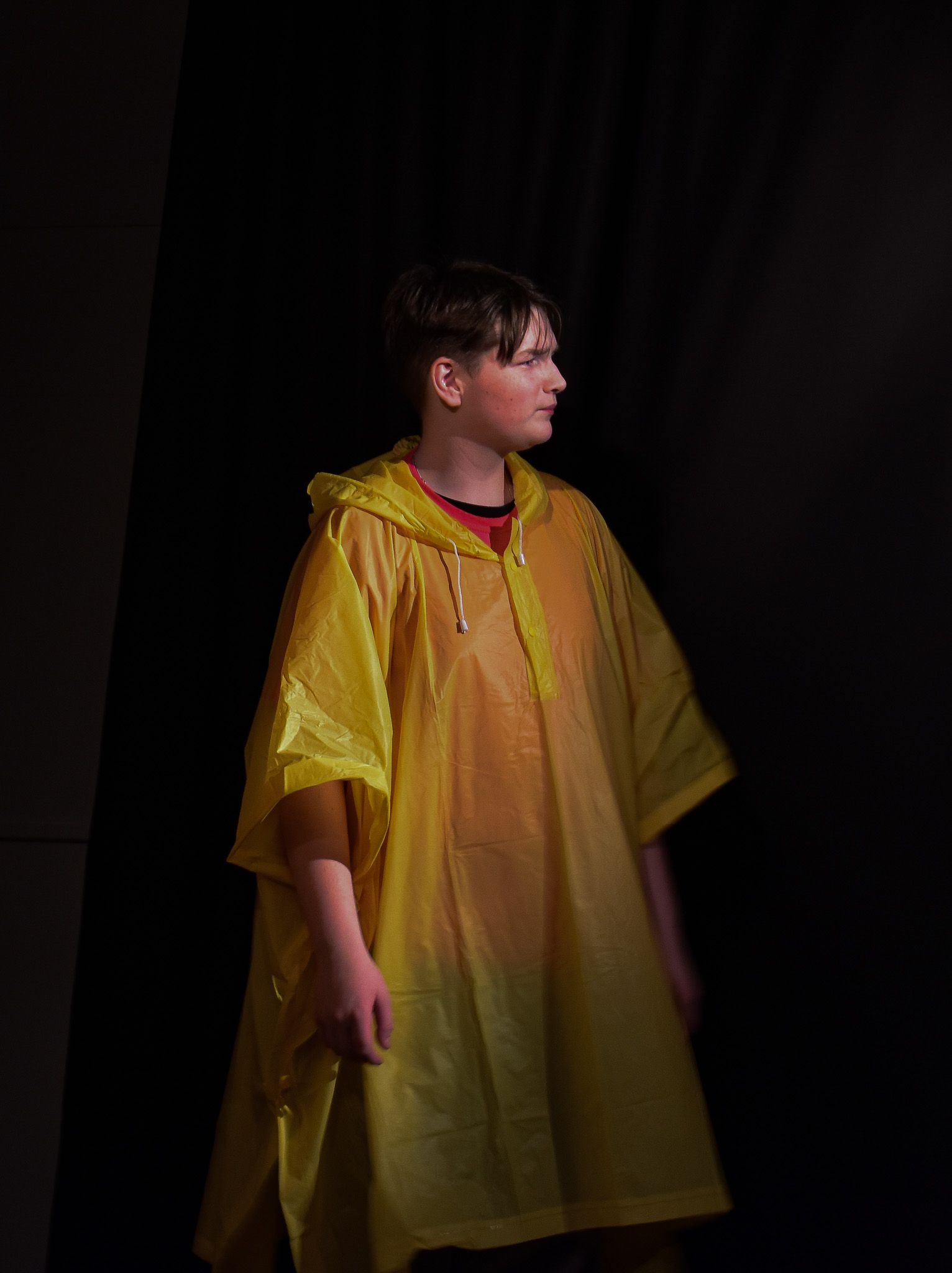 A young man wearing a yellow raincoat is standing in a dark room.