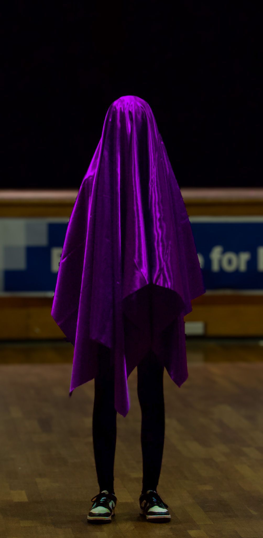 A person is standing in a dark room with a purple cloth covering their face.