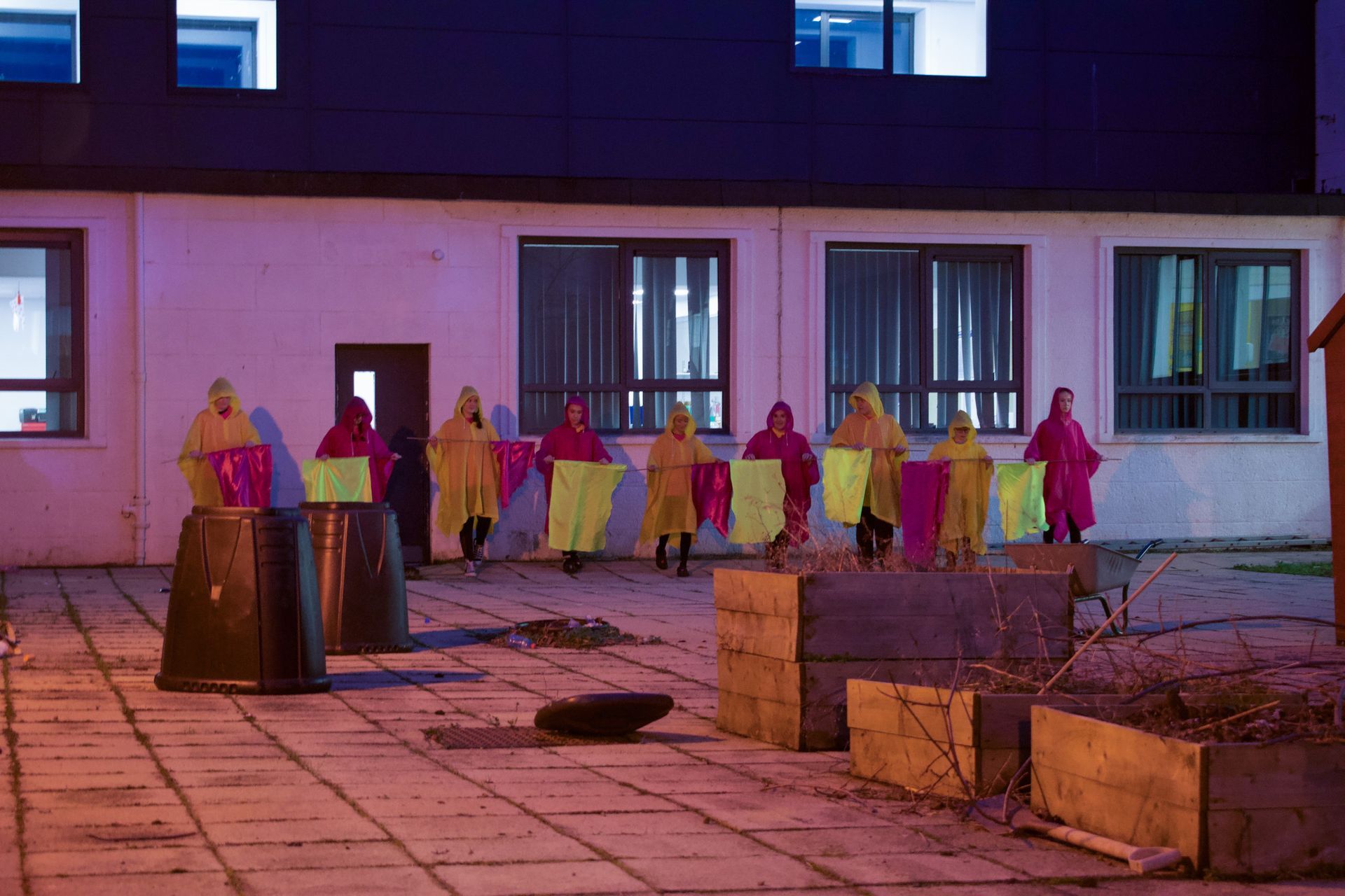 A group of people in pink and yellow raincoats are standing in front of a building.