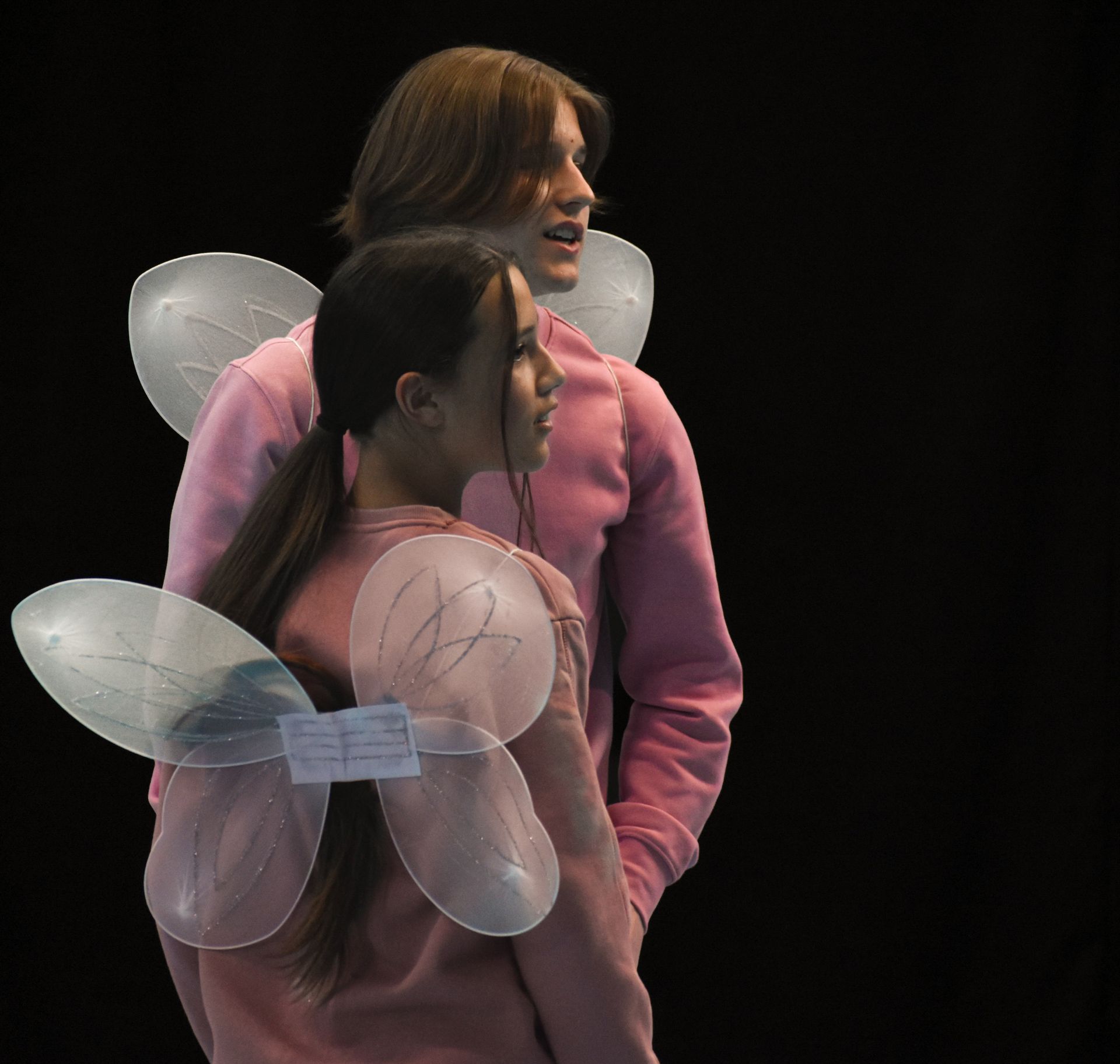 Two teenagers in pink with translucent angel wings, posed against a black background.