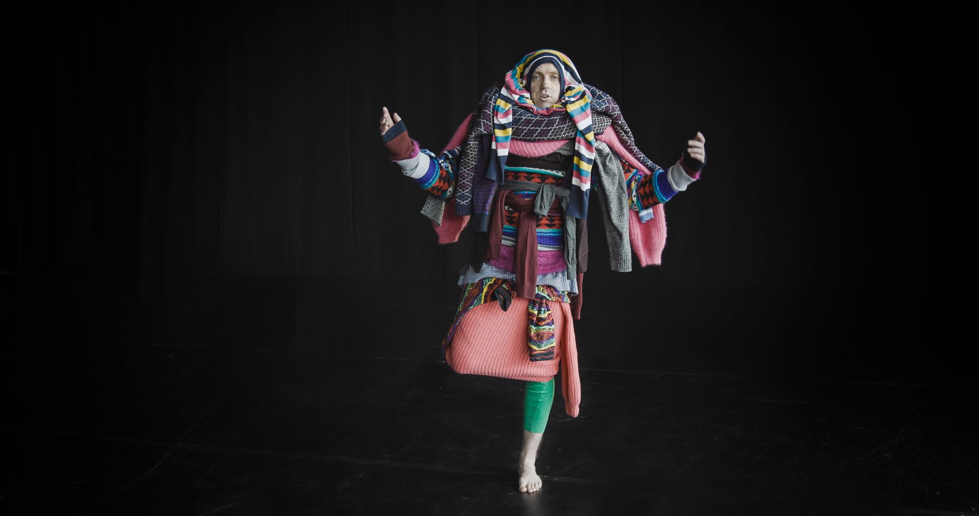 A man is wearing multiple jumpers and standing on one leg.