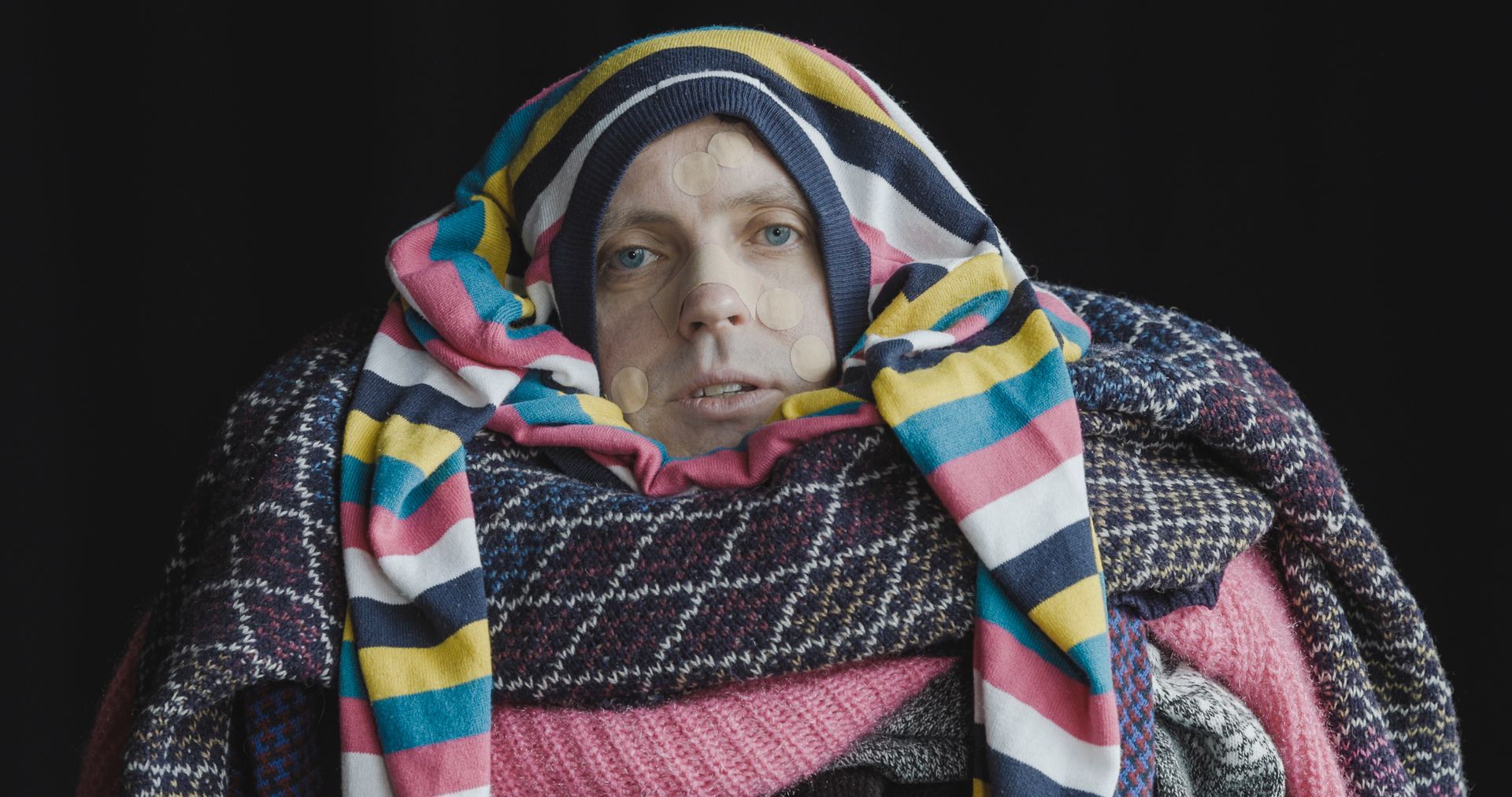 A man is wrapped in several jumpers around his body and head.