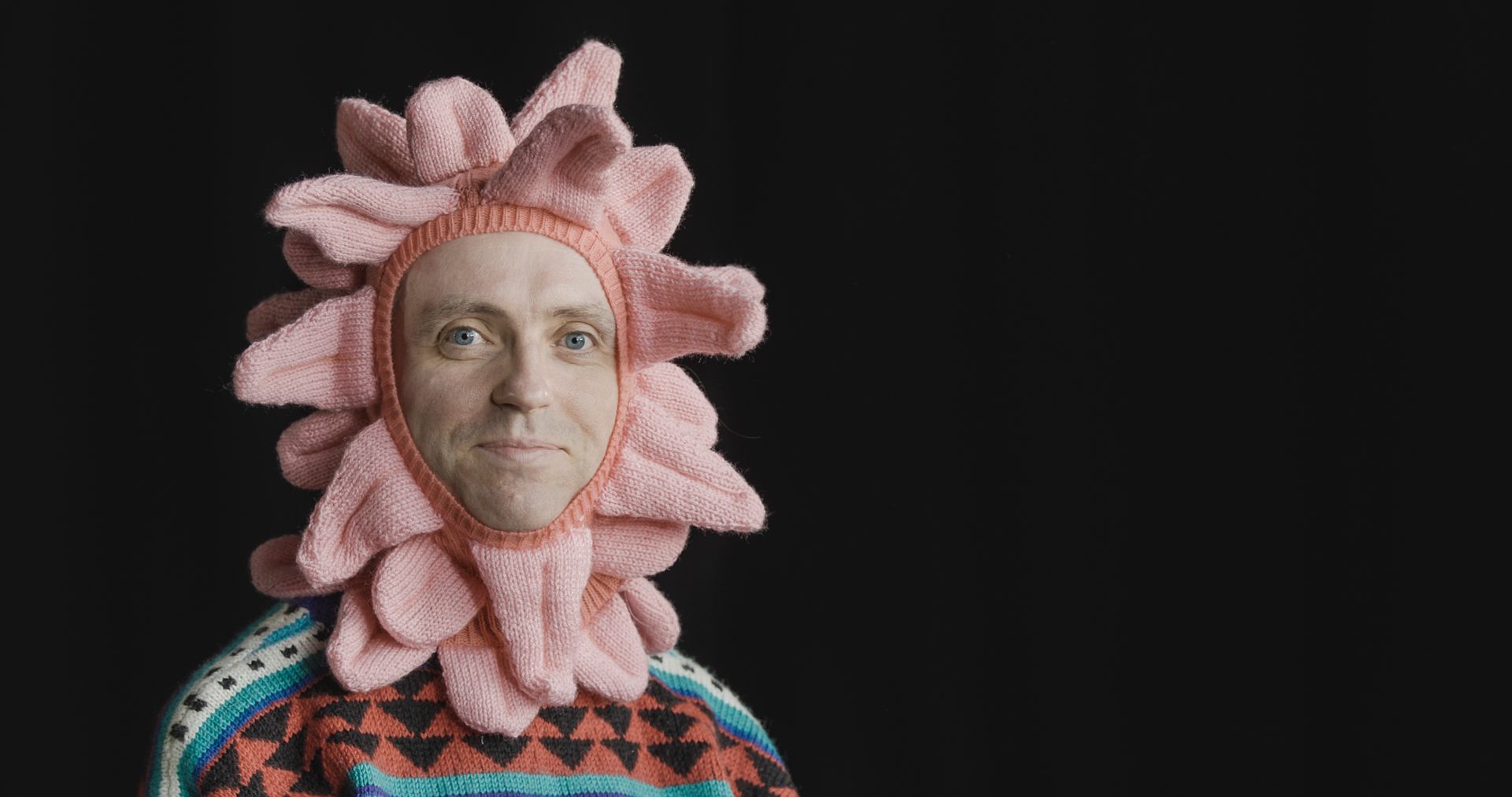 A man is wearing a pink knitted tongue hat on his head.