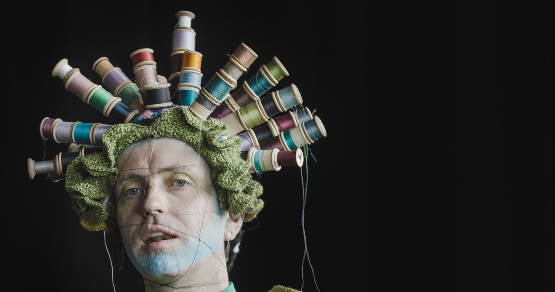 A man with a bunch of spools of thread on his head.
