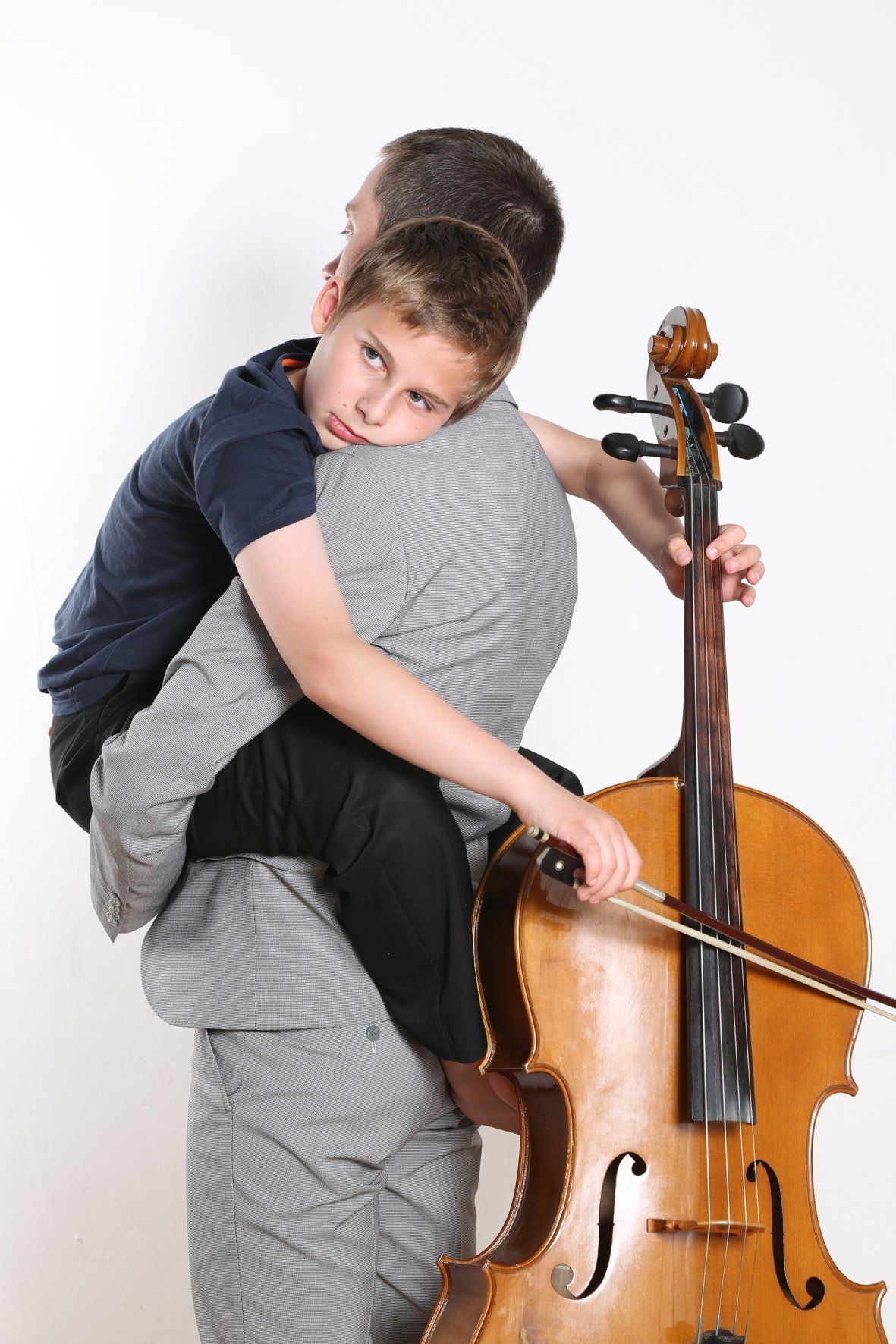 A man is holding a child who is playing a cello.