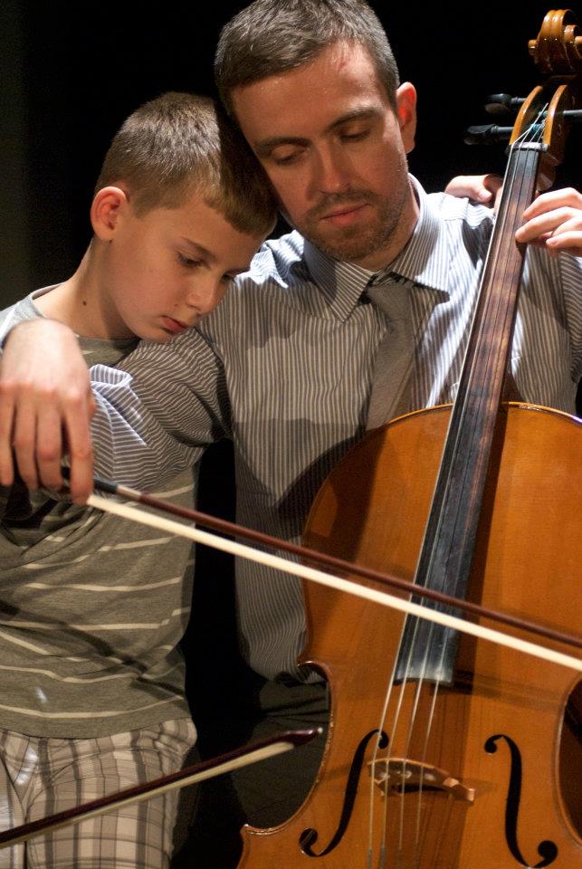 A man is teaching a young boy how to play a cello.