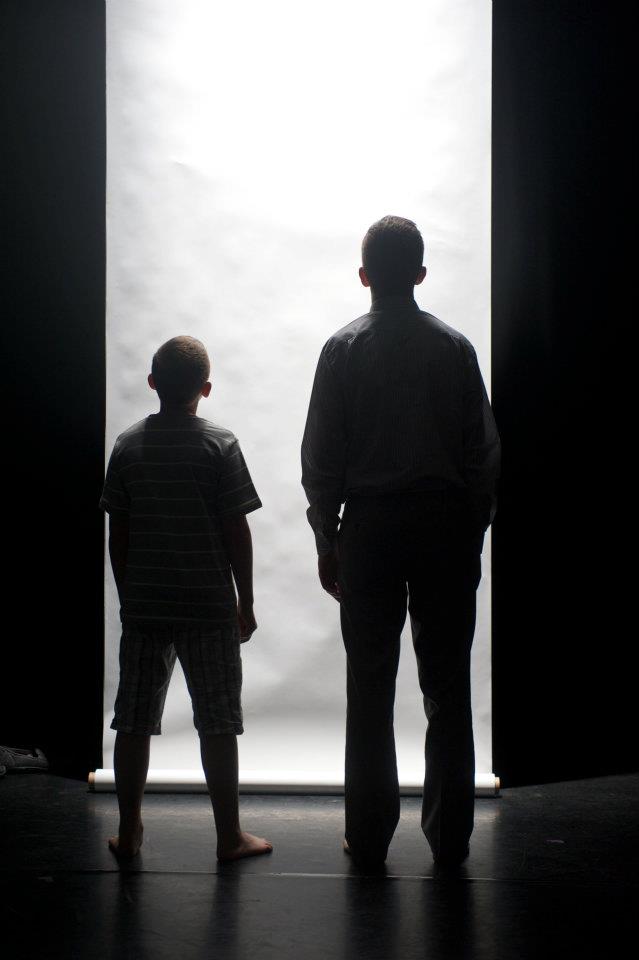 A man and a boy are standing in front of a white wall.