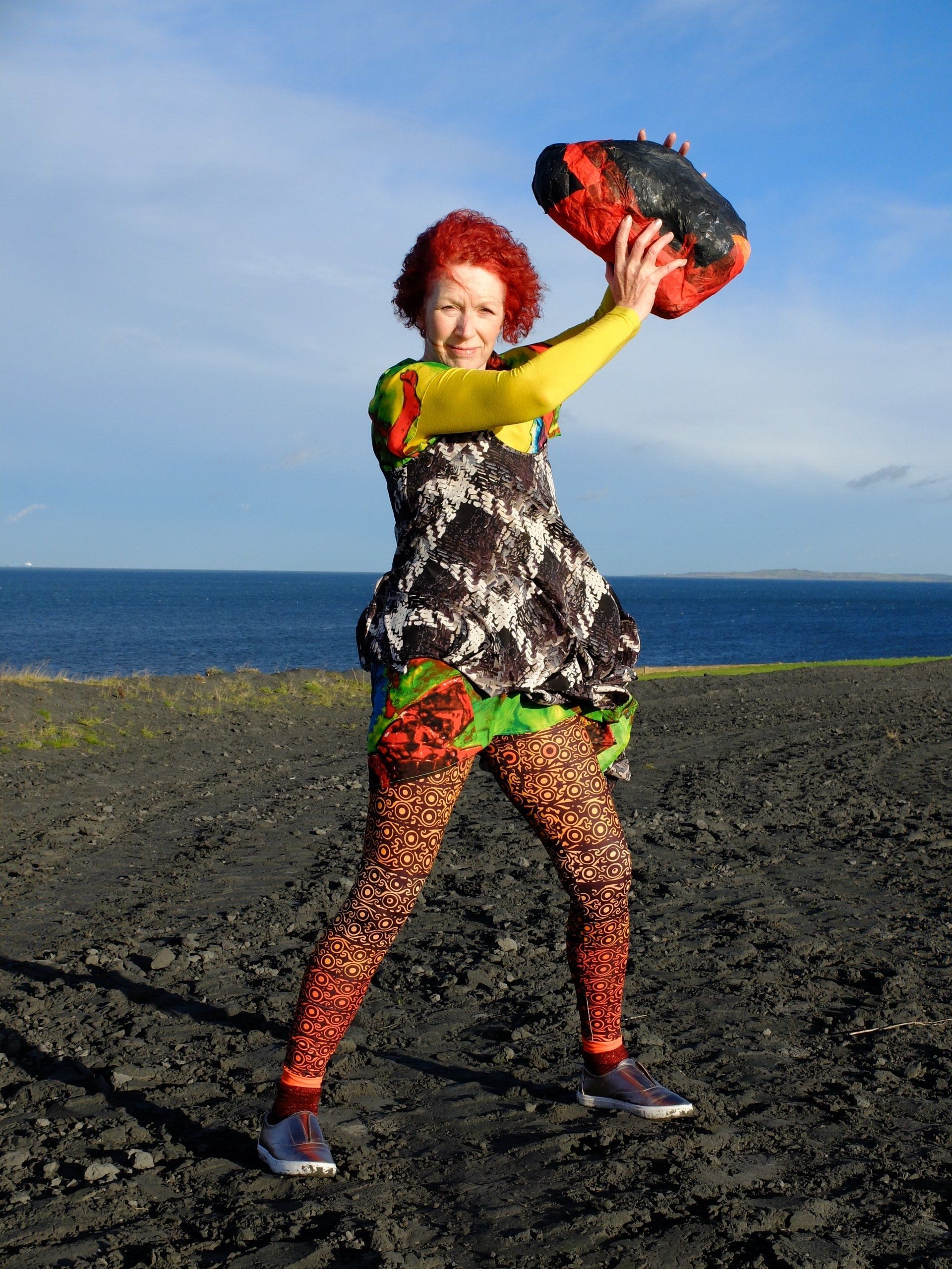 A woman in a colorful dress is holding a red bag over her head
