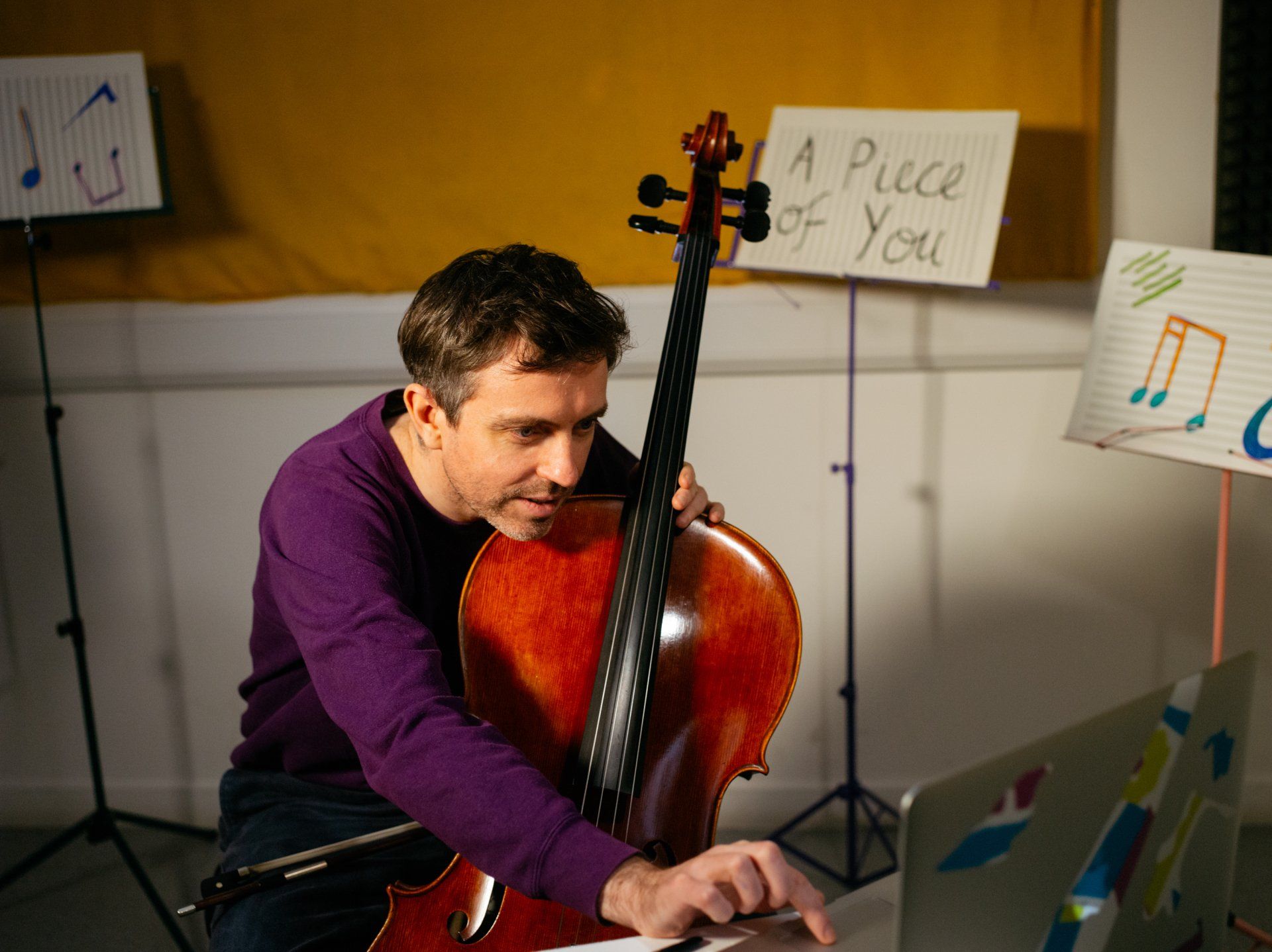A man is playing a cello in front of a sign that says a piece of you