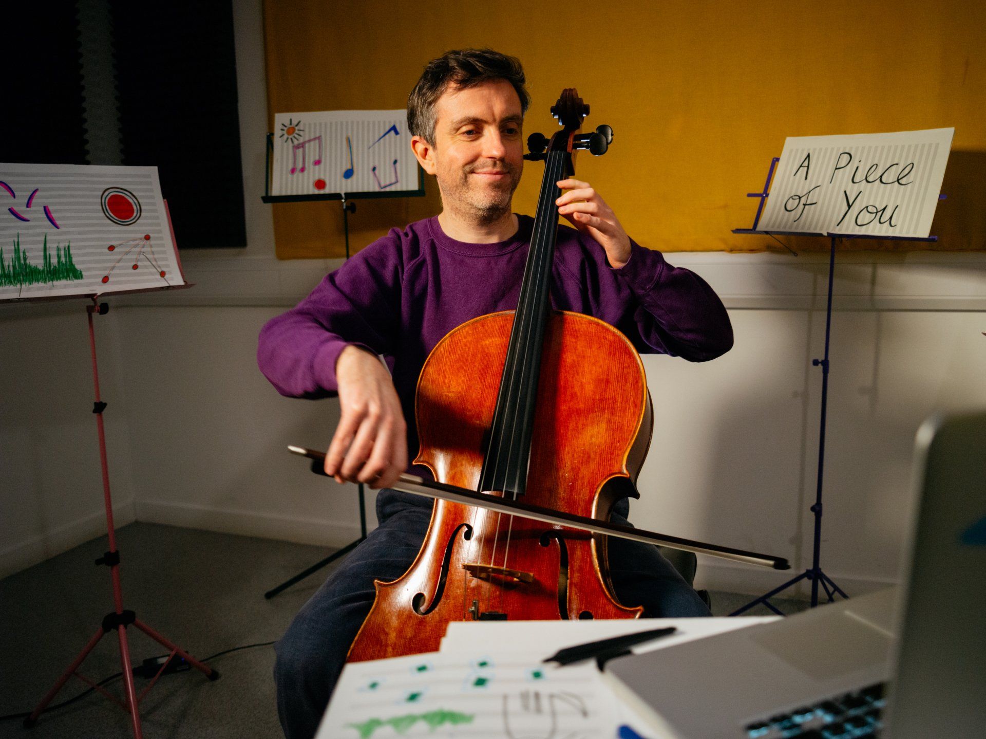A man is playing a cello in front of a sign that says a piece of you