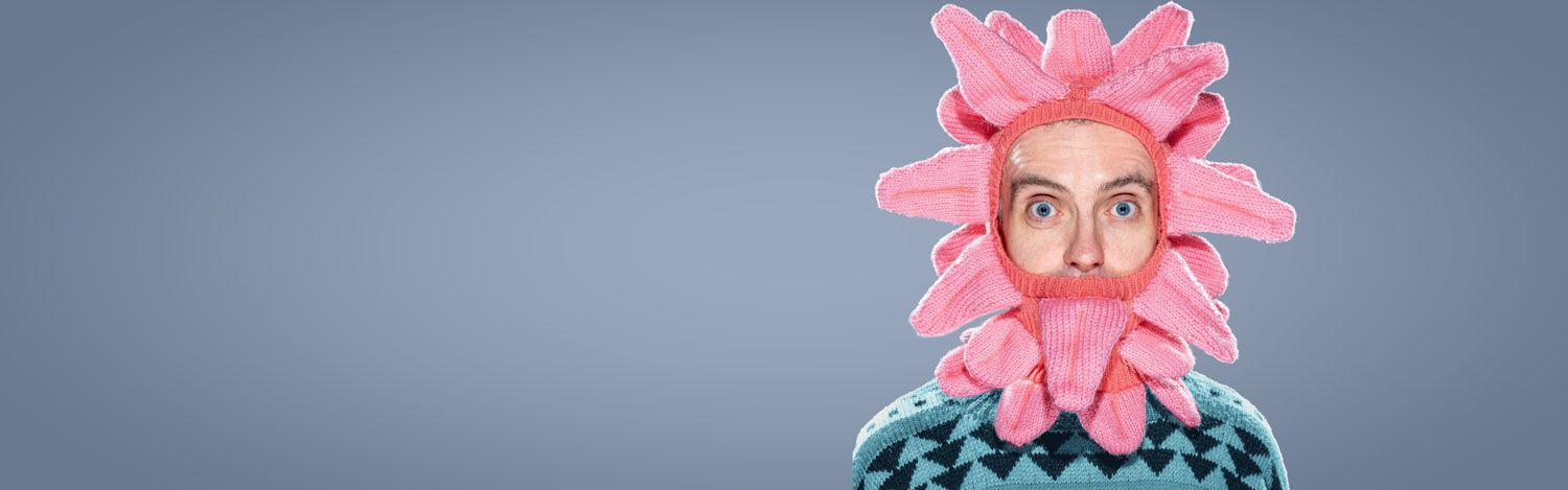 Person peeking through a pink balaclava of knitted tongues against a gray background