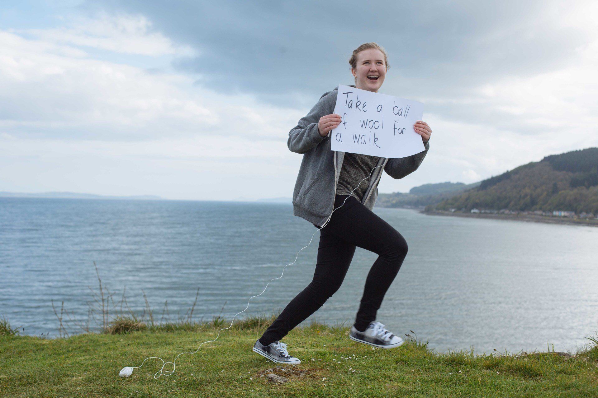 A girl is holding a sign in front of the ocean.