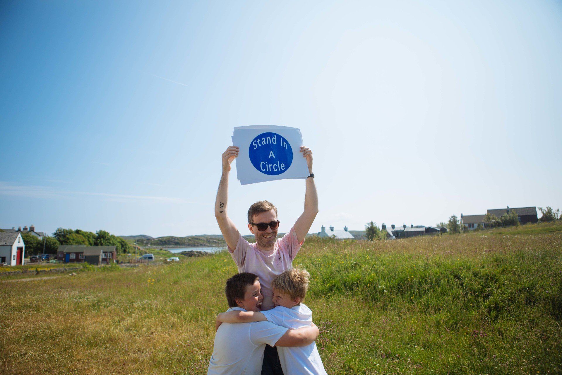 A group of people are hugging and holding a sign in a field.
