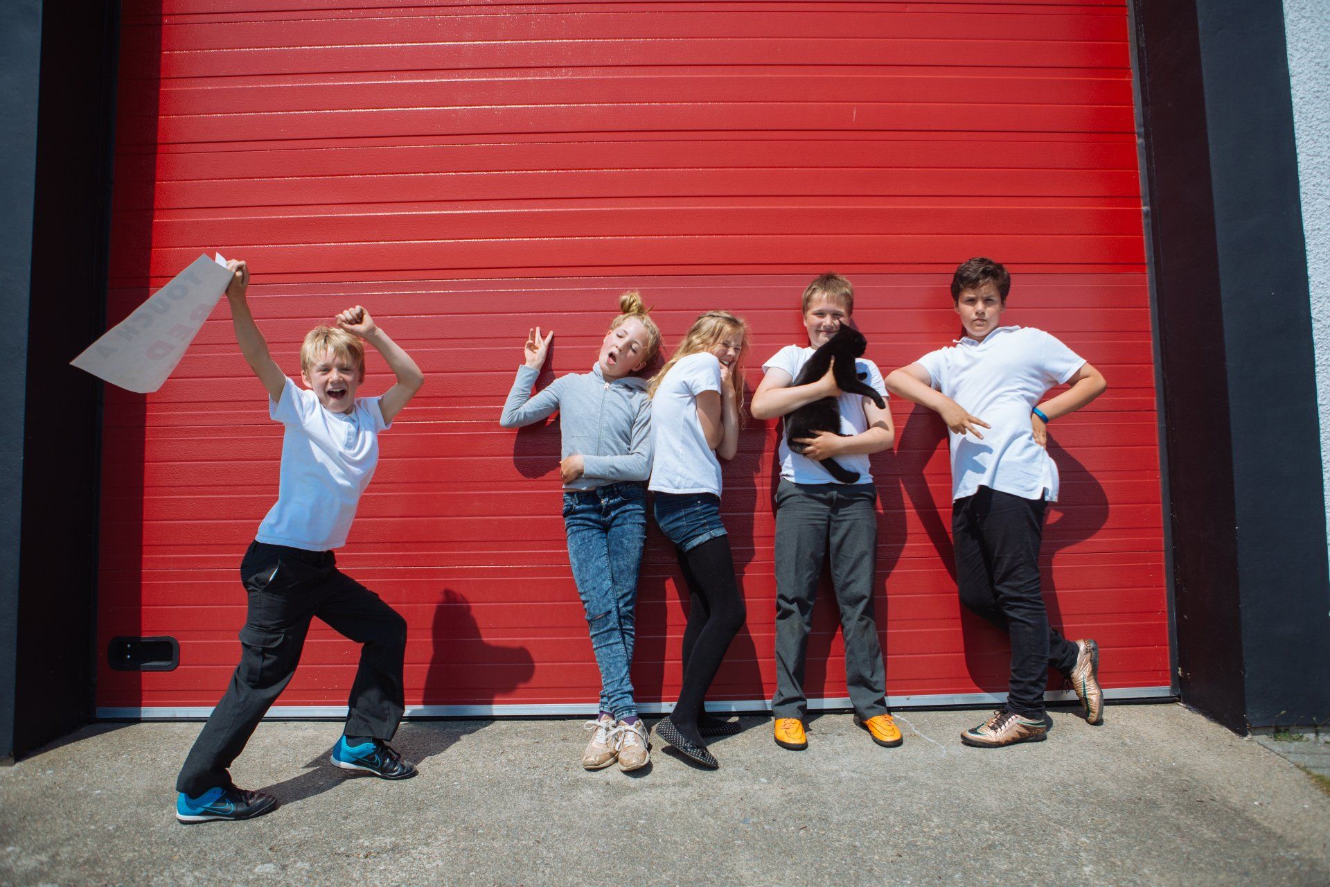 A group of children are posing for a picture in front of a red garage door.
