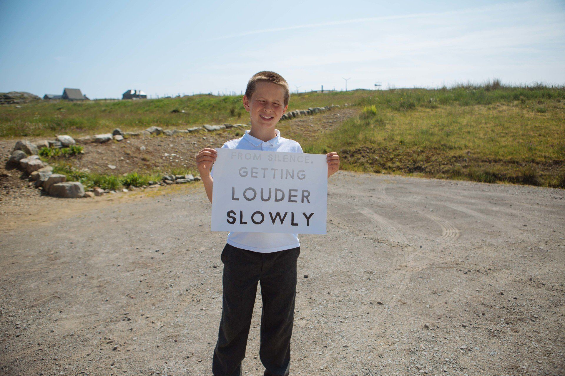 A young boy is holding a sign that says getting louder slowly